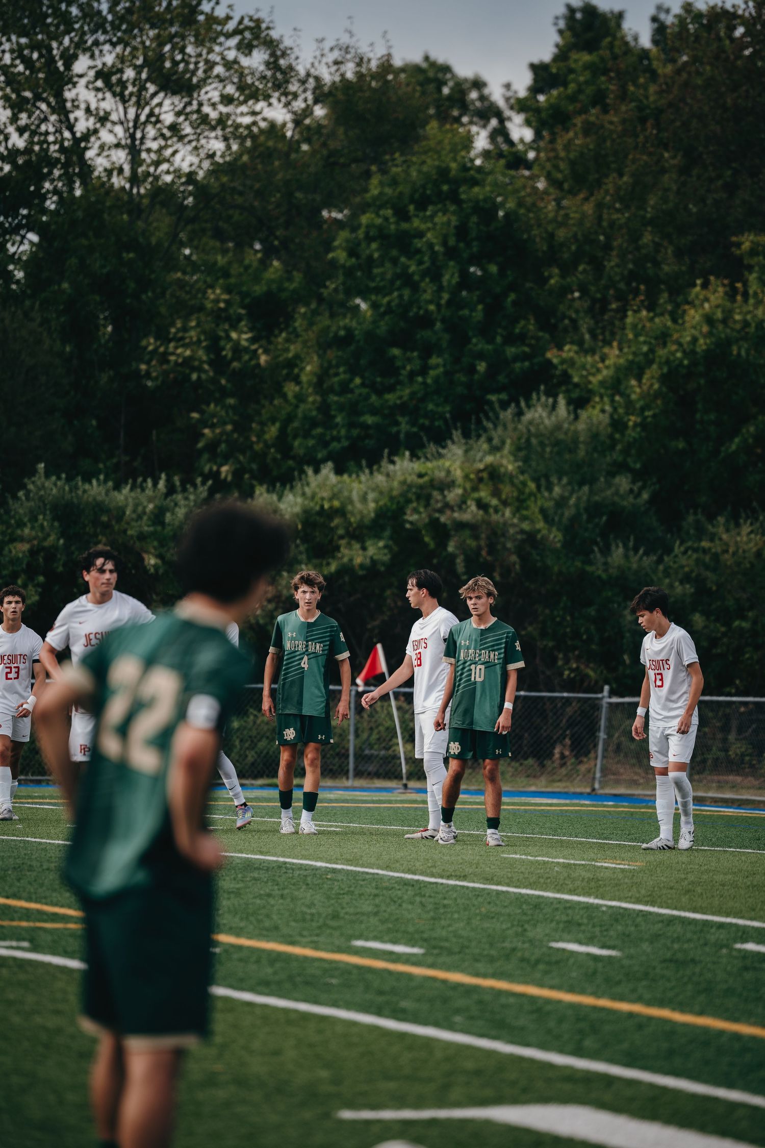Youth soccer players in green and white uniforms compete on a turf field during an evening match.