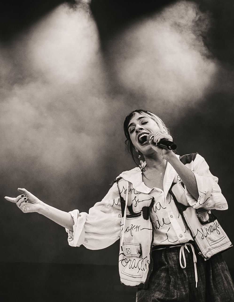 Black and white photo of a female singer performing on stage, holding a microphone and gesturing dramatically under stage lights.