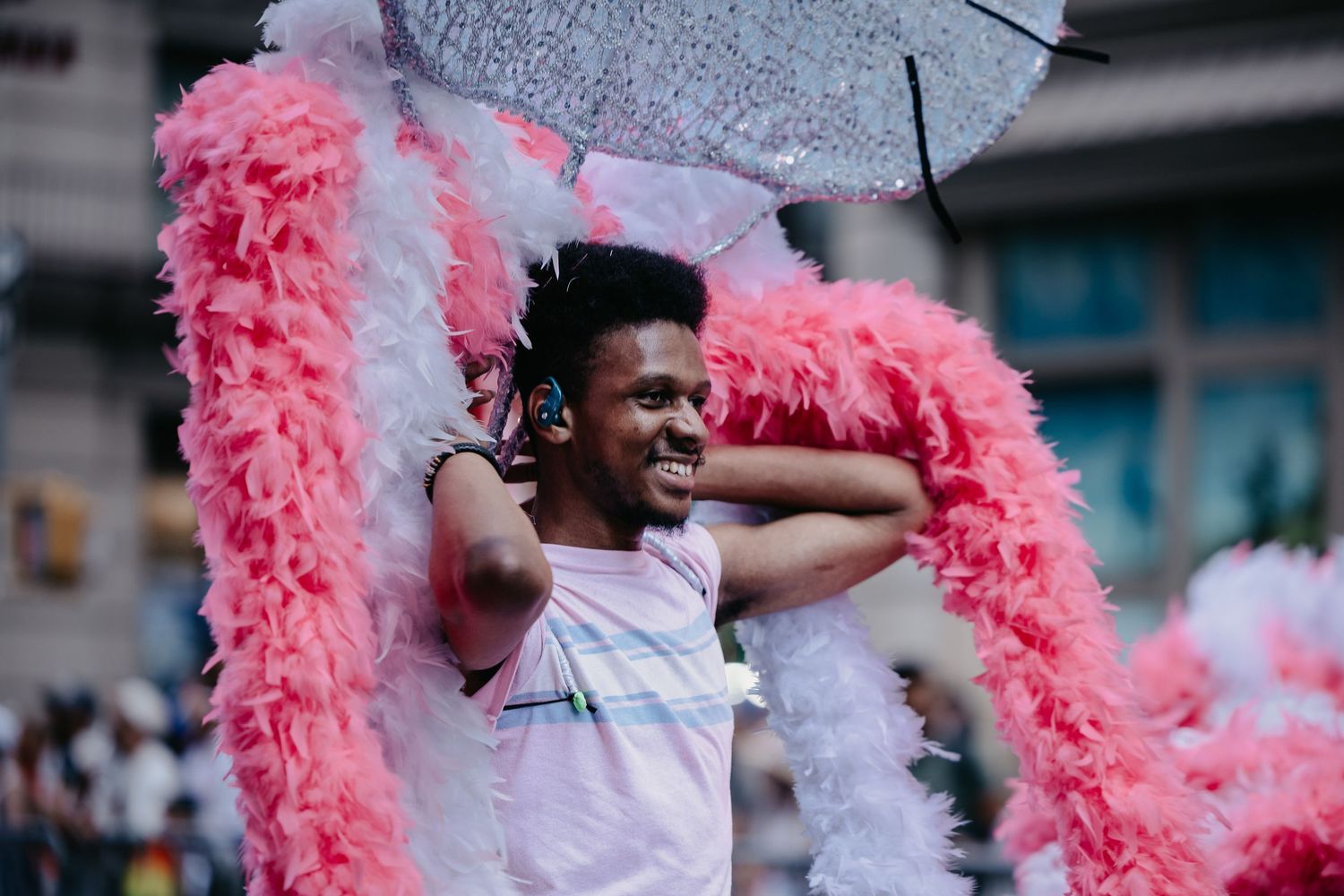 Smiling man adorned with pink feather boas celebrating at a Pride parade.