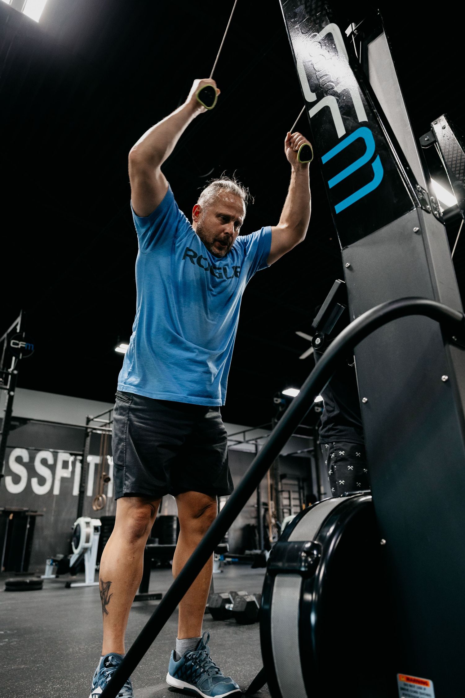 Man in blue shirt performing cable exercise on gym machine at CrossFit facility.