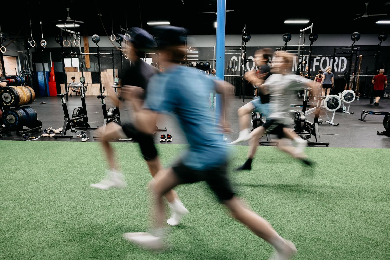 People running and exercising with motion blur in a CrossFit gym with green turf flooring.