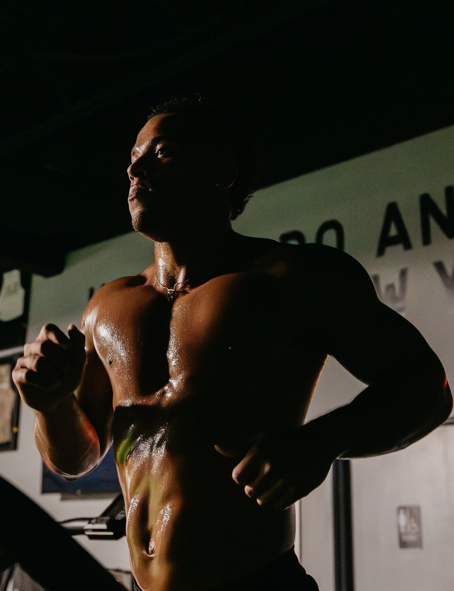 Sweaty shirtless muscular man running on treadmill in dark gym, intense cardio workout session.
