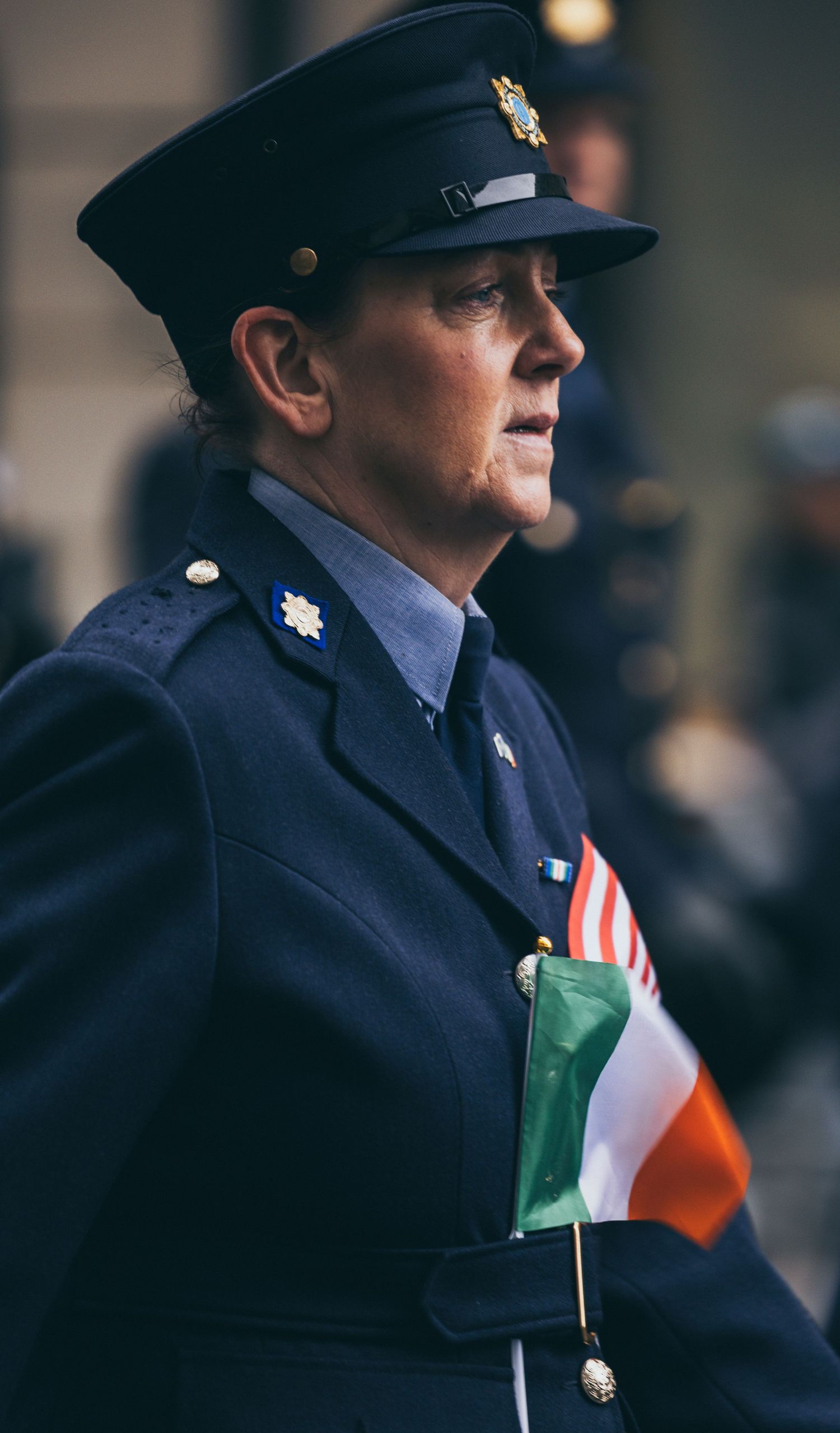 Female officer in navy blue uniform holding an Irish tricolor flag at a formal parade.