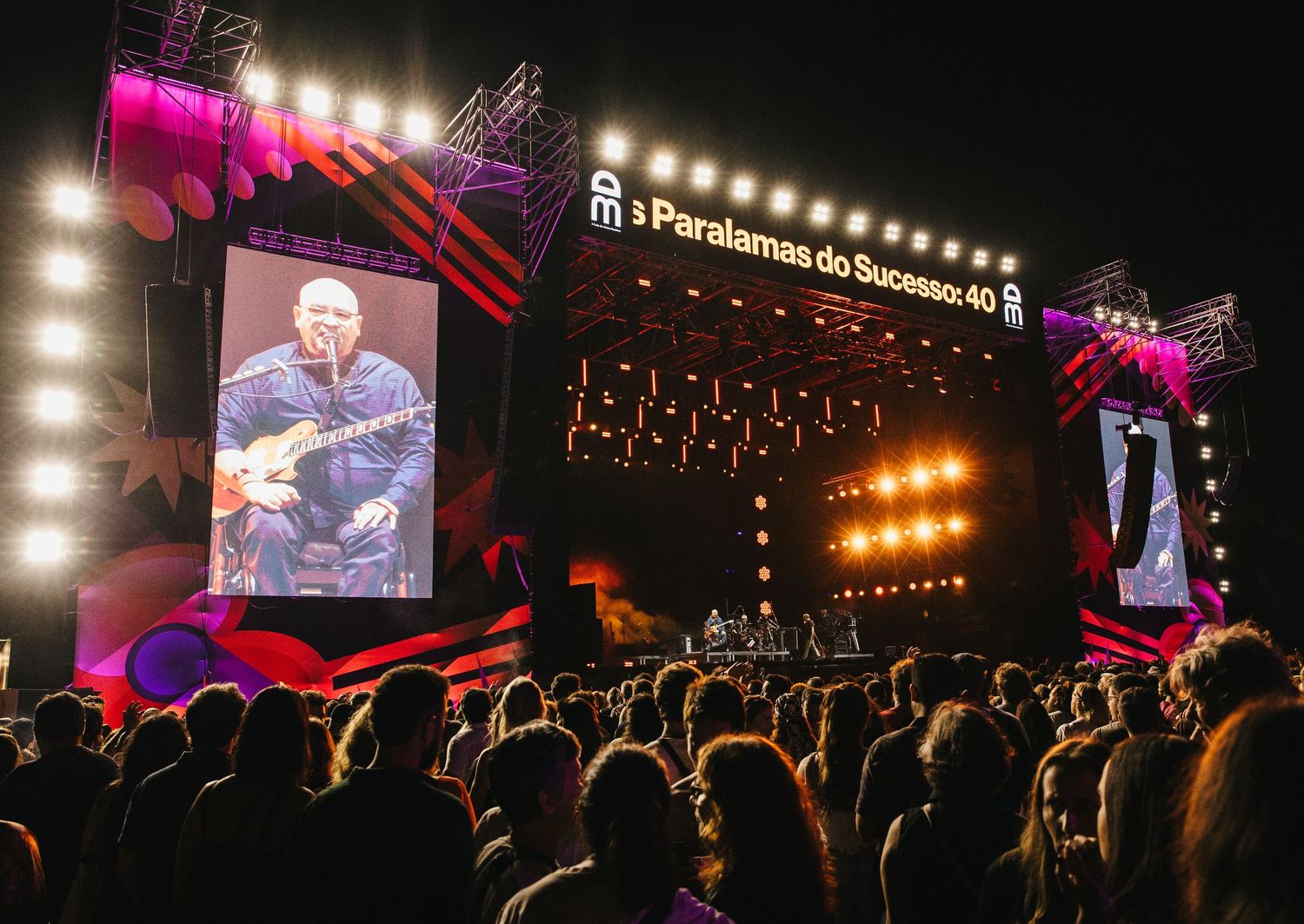 Paralamas do Sucesso 40th anniversary concert with large LED screen displaying guitarist on stage at night.