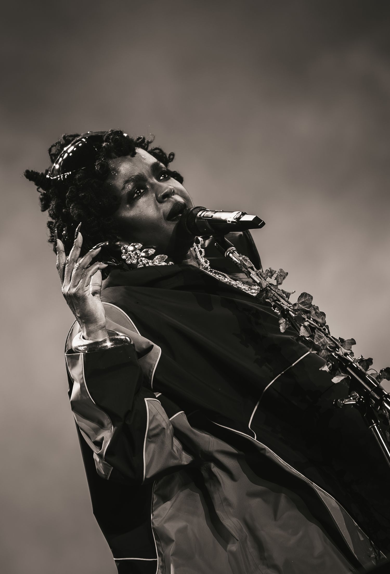 Black and white photo of a female singer performing on stage, holding a microphone while wearing an ornate jacket.
