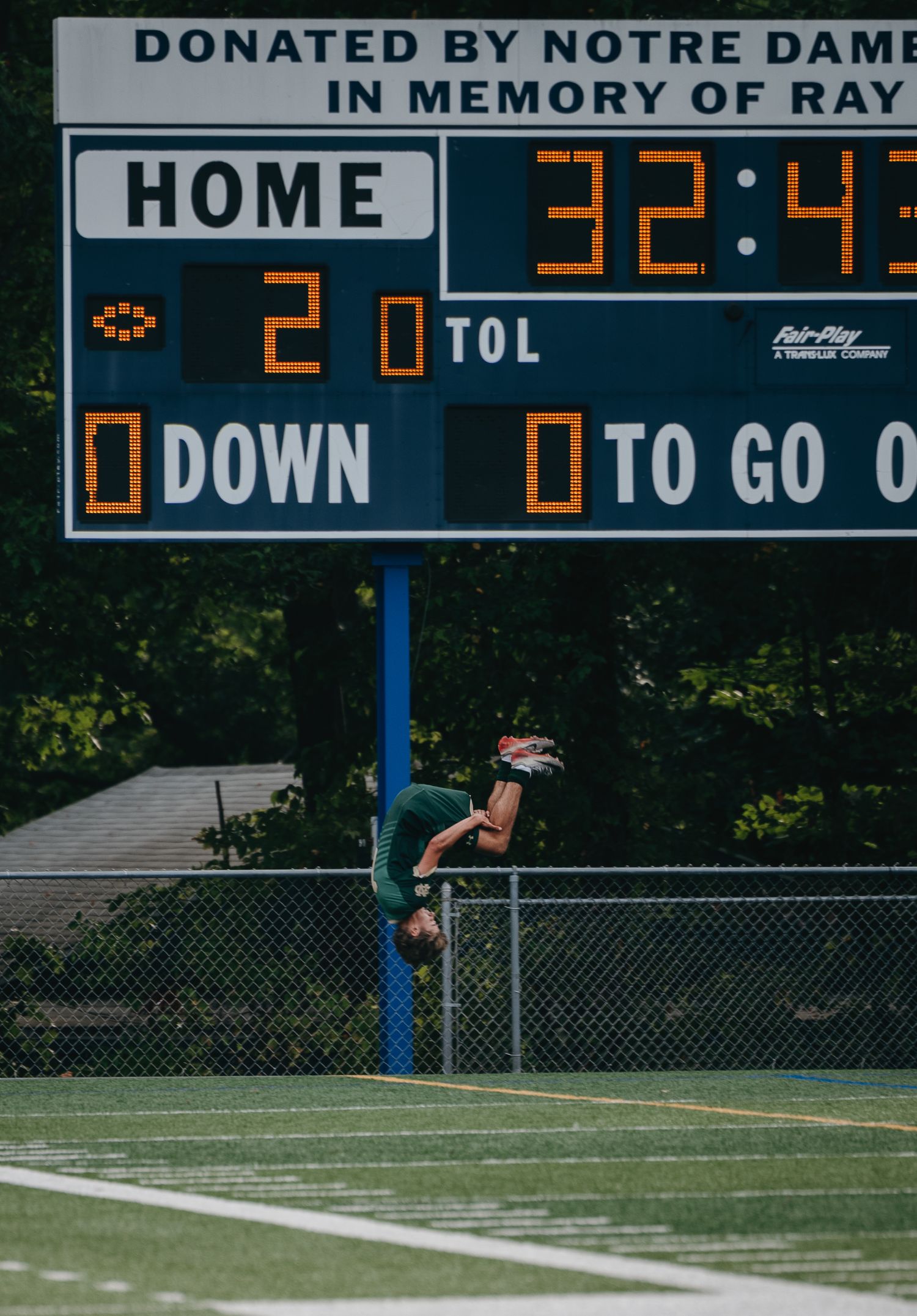 Athlete performs a backflip near a football scoreboard donated by Notre Dame, showing 32:43 on the clock.