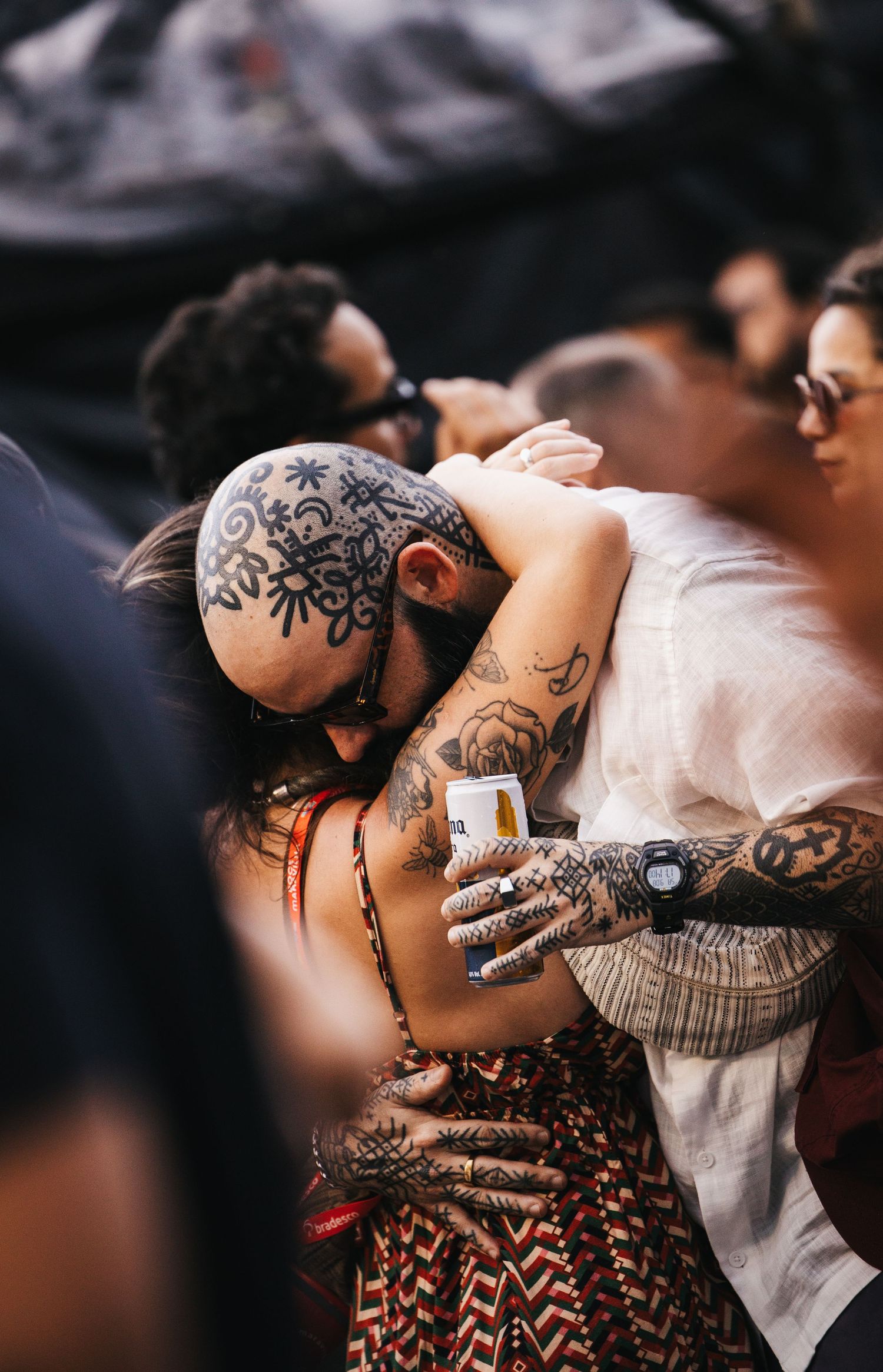 Heavily tattooed couple embracing at outdoor festival, man with tribal head tattoos hugging woman in crowd.