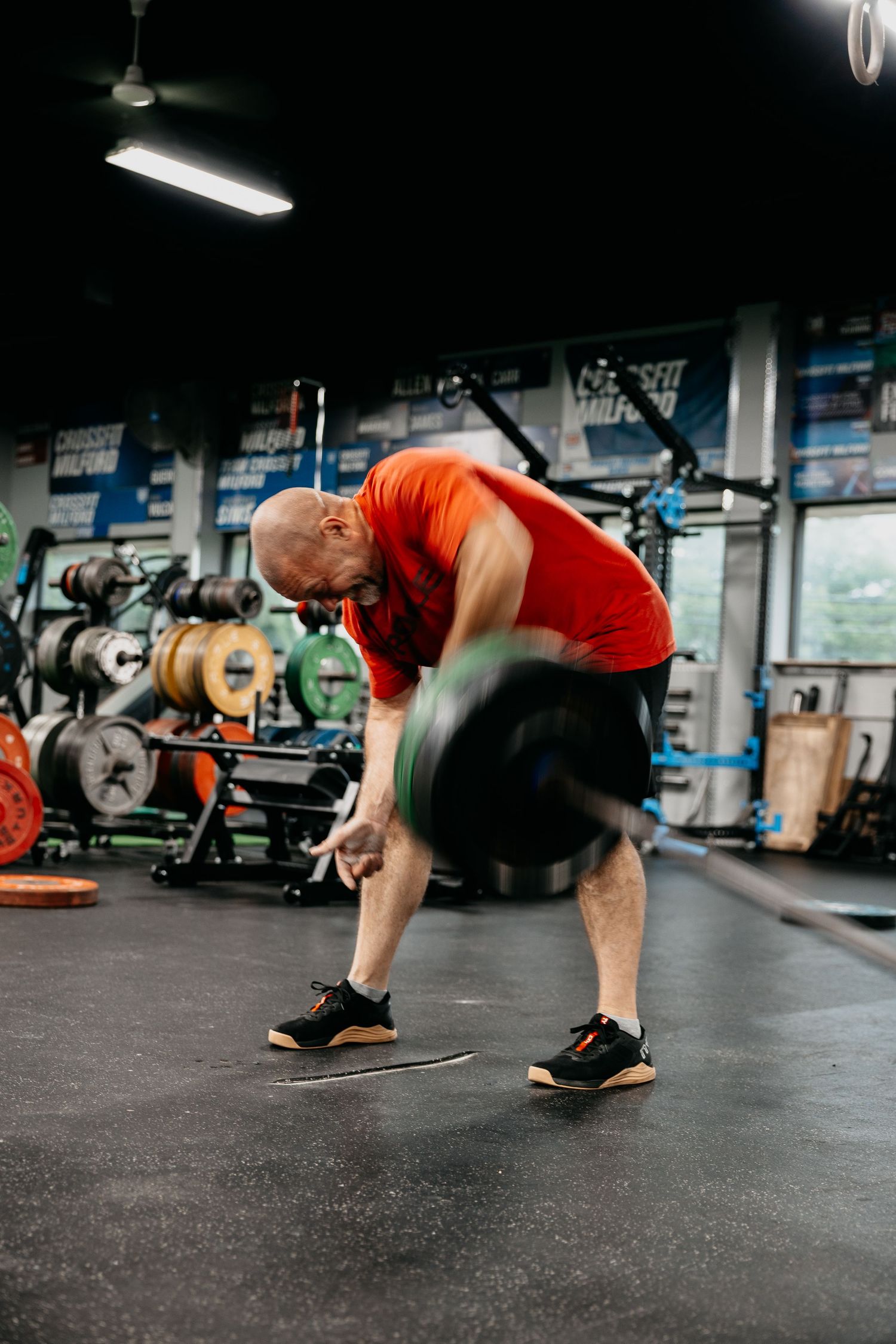 Bald man in red shirt doing deadlift exercise with barbell in CrossFit gym.