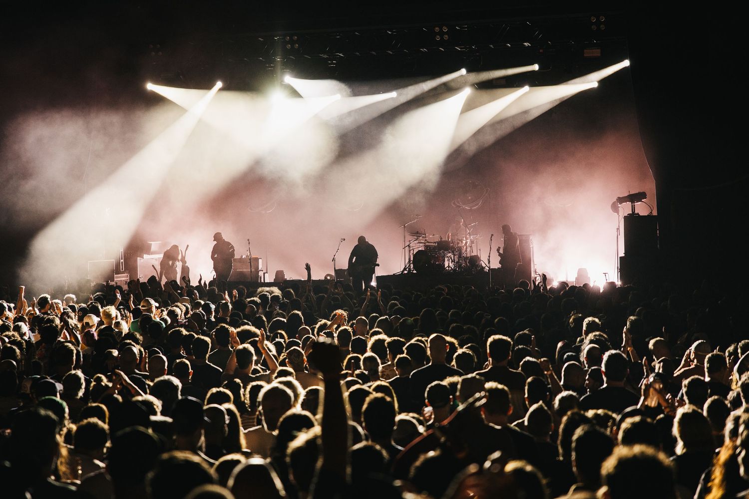 A massive crowd watches performers on a dramatic fog-filled stage with bright white spotlights at a concert.
