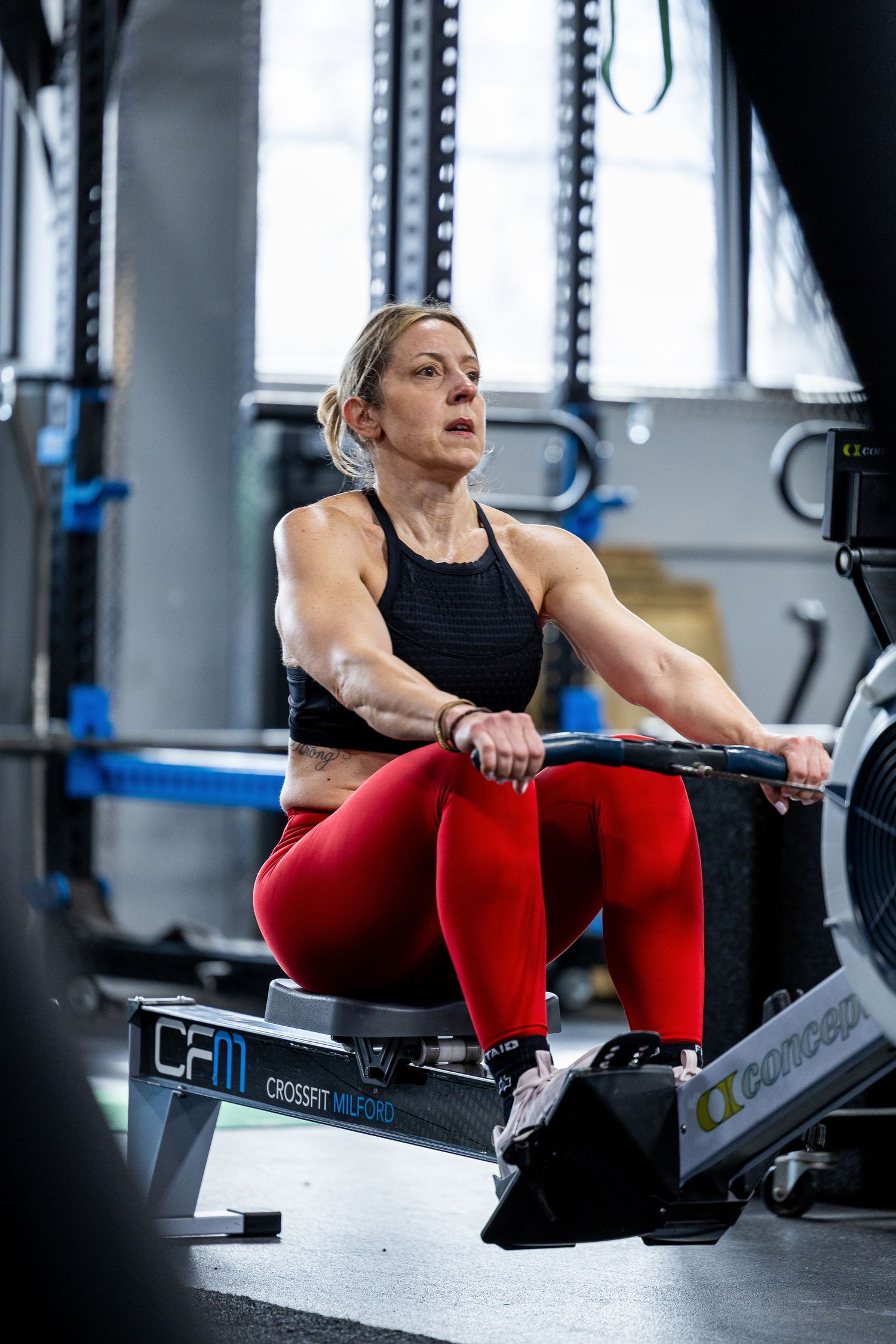 Muscular woman in red leggings intensely rowing on a Concept2 machine at CrossFit Merido gym.