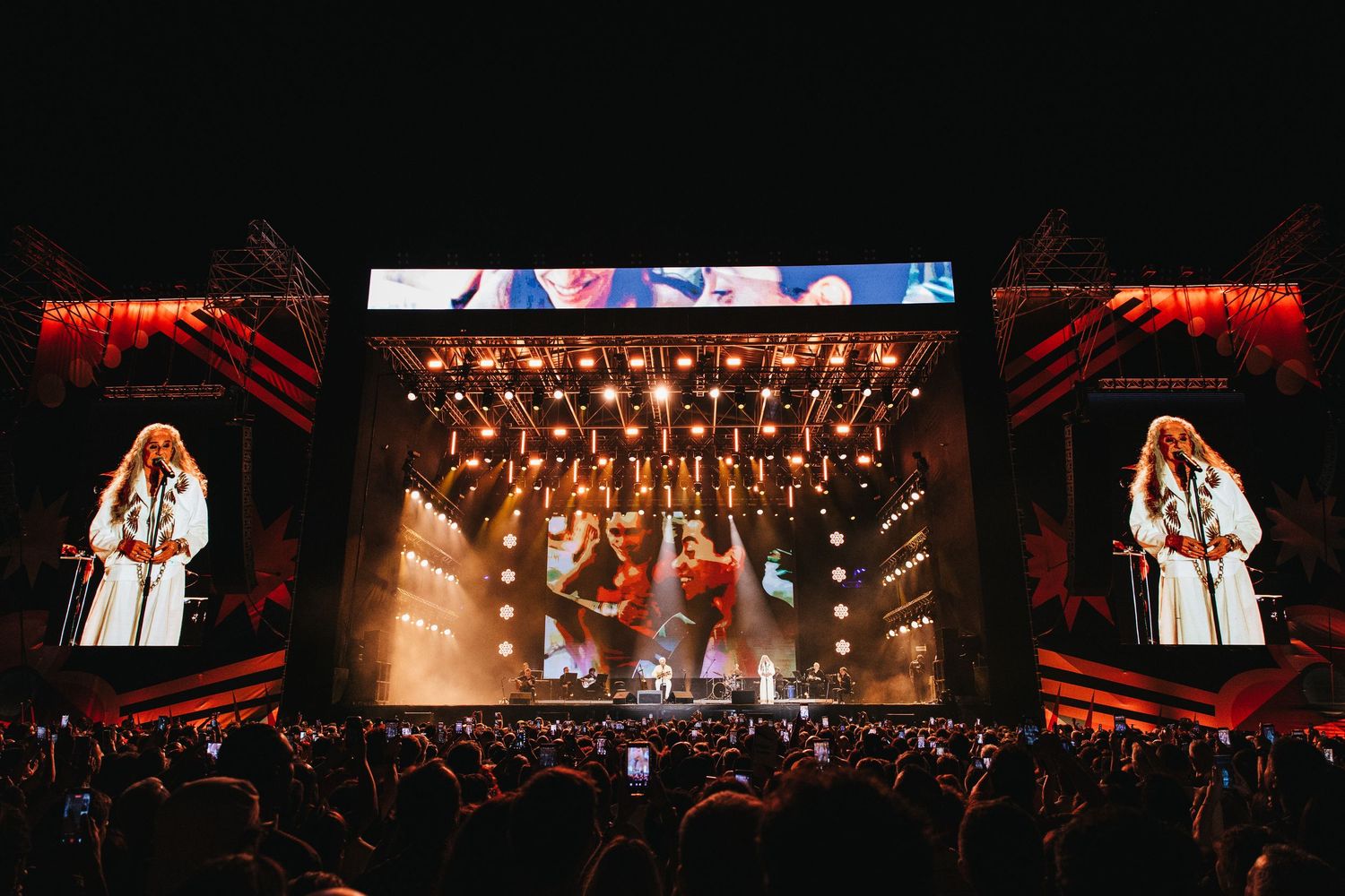 Outdoor concert stage with large LED screens displaying performers at a night music festival.