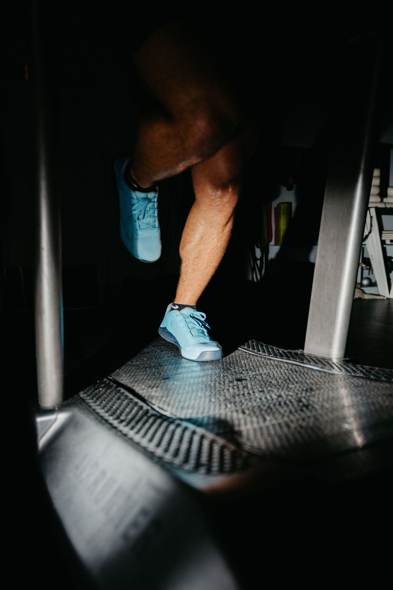 Person in light blue sneakers stepping on a treadmill in a dark gym setting.