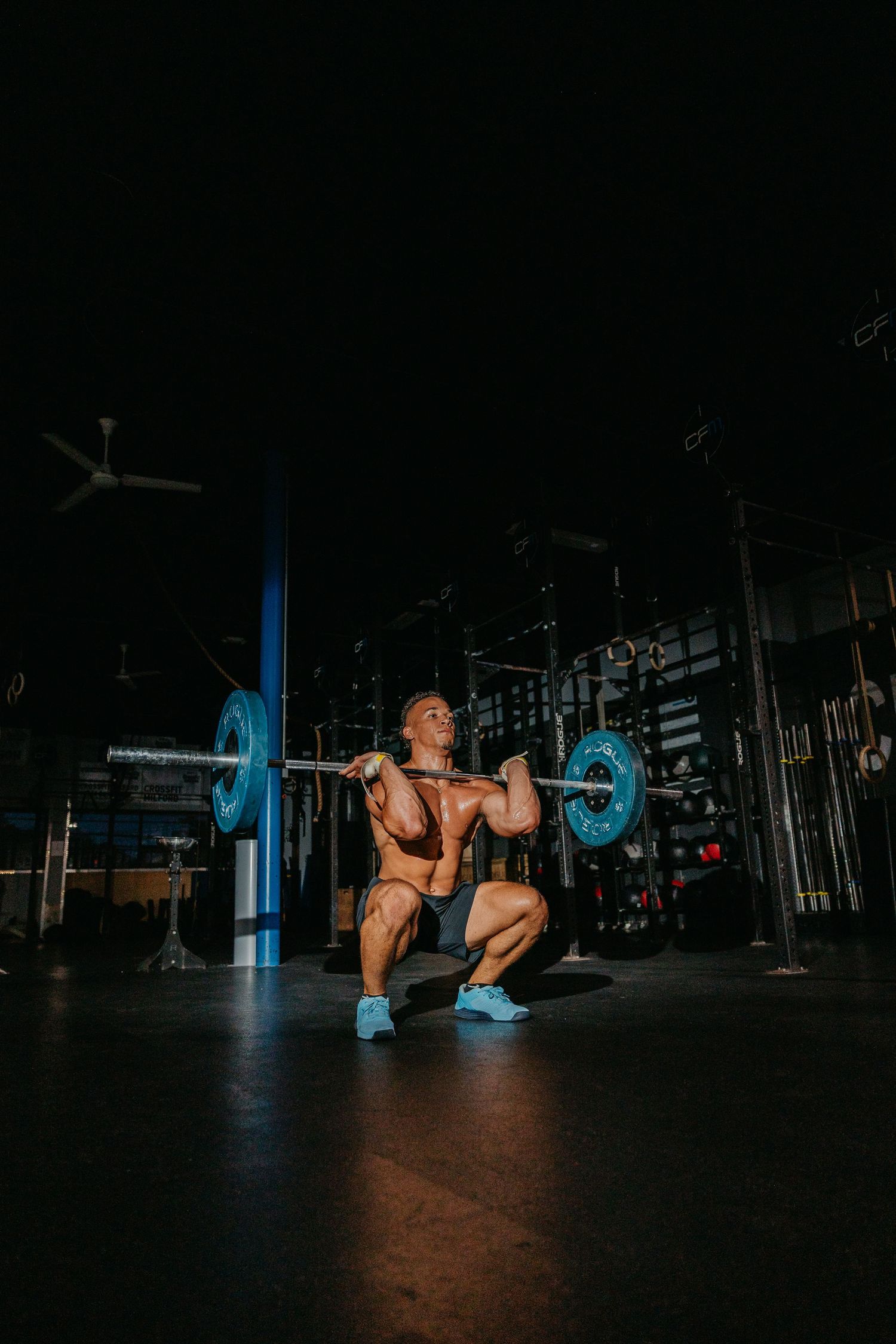 Muscular bodybuilder performing a heavy barbell back squat in a dark gym wearing blue shoes.