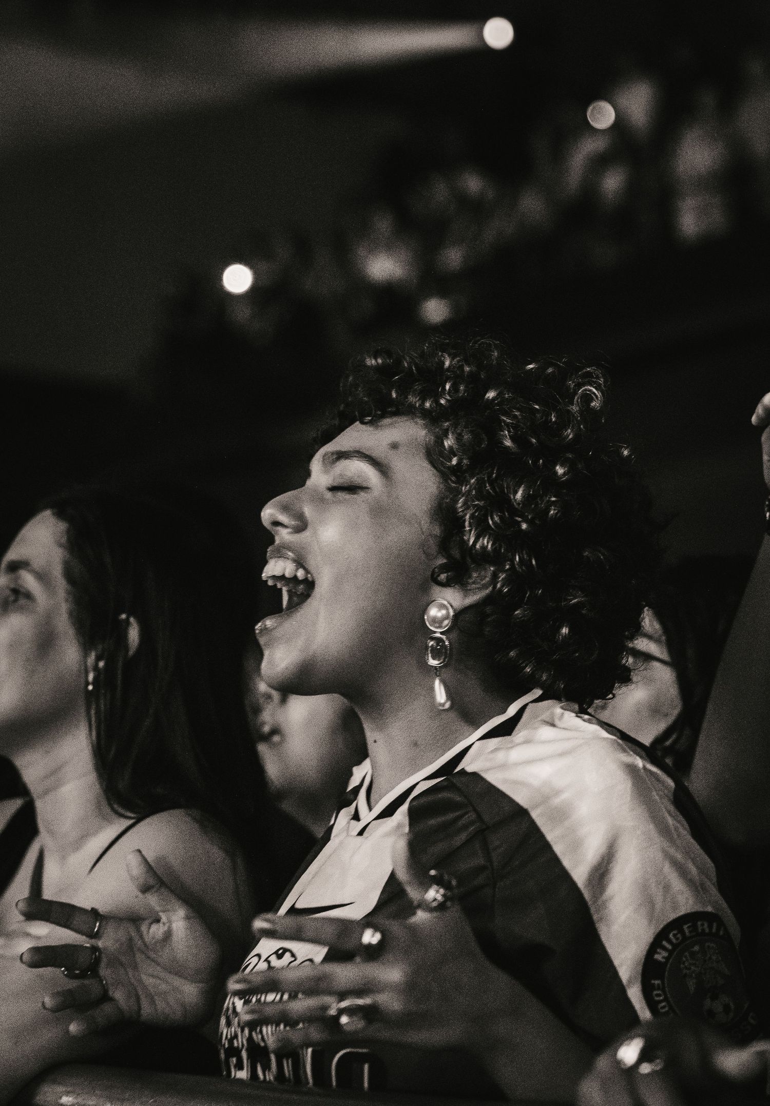 Black and white close-up of an enthusiastic female concert fan singing with mouth wide open.