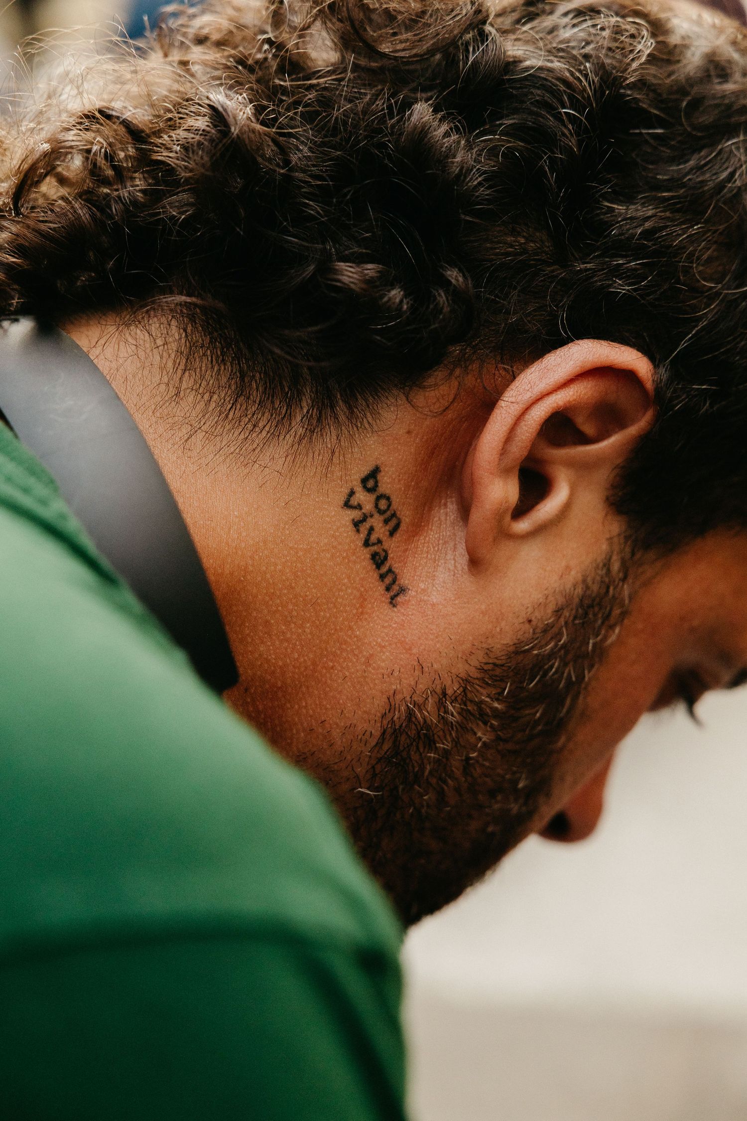 Man with curly hair and bon vivant neck tattoo wearing headphones and green shirt.