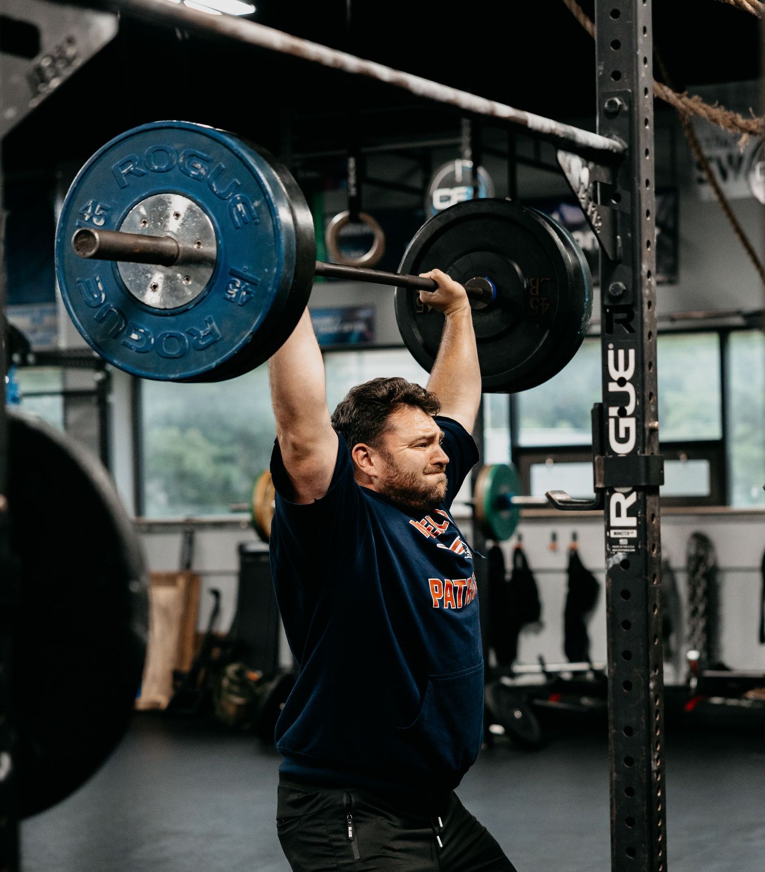 Man performing overhead barbell press in a gym, lifting heavy weights above his head during a strength training workout.