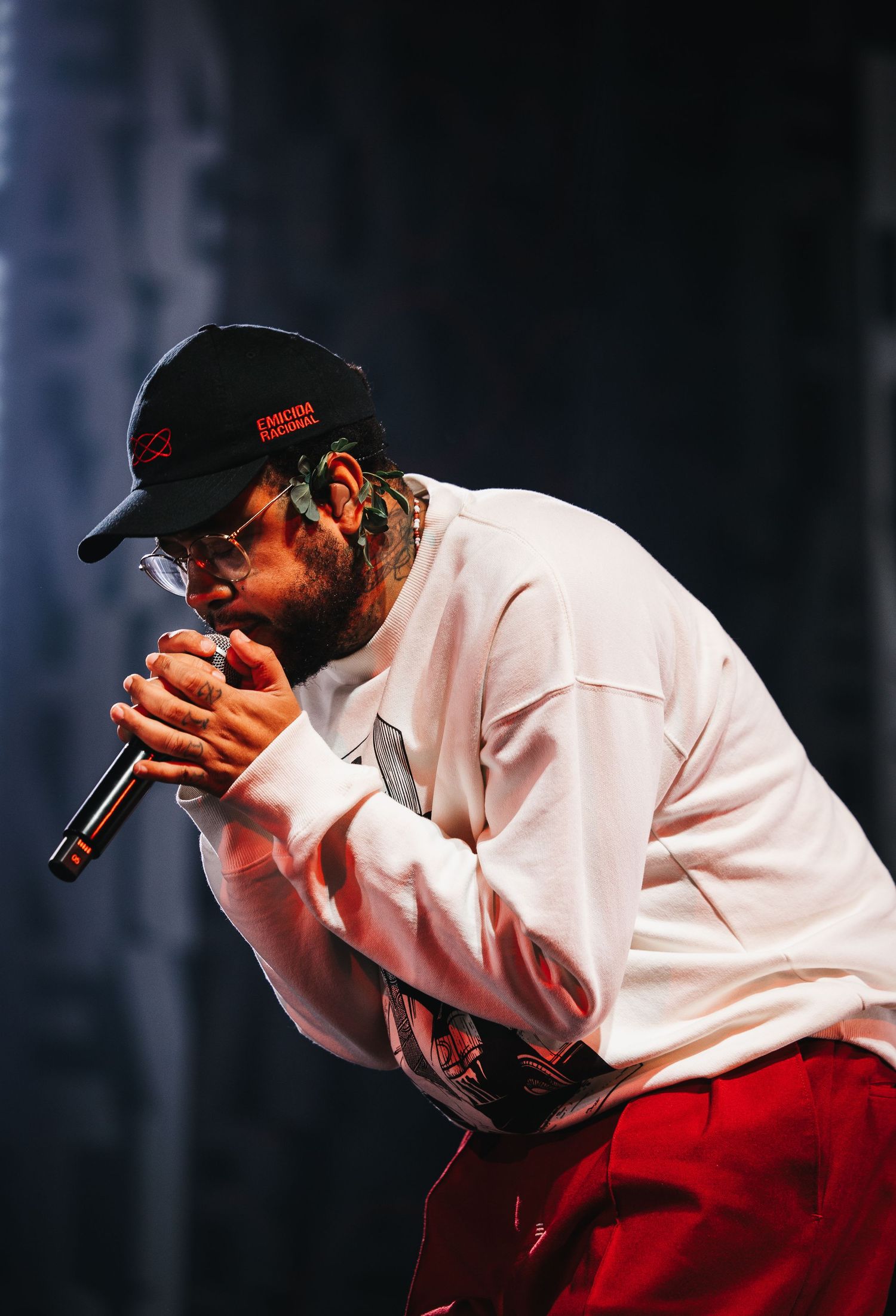 Male hip-hop artist in white sweatshirt and red pants performs on stage holding microphone.