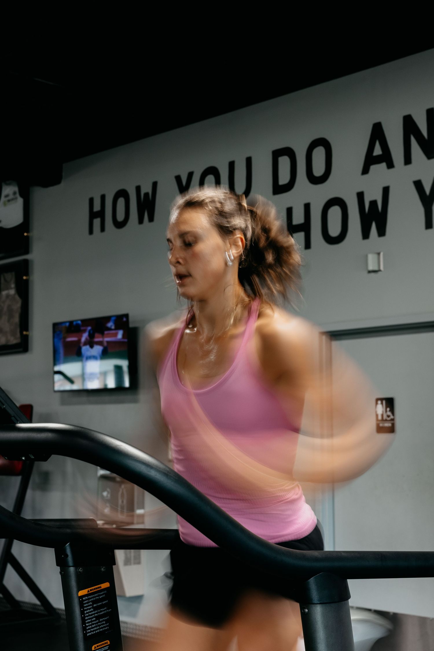 Woman in pink tank top running on treadmill at gym, motion blur capturing intense cardio workout session.