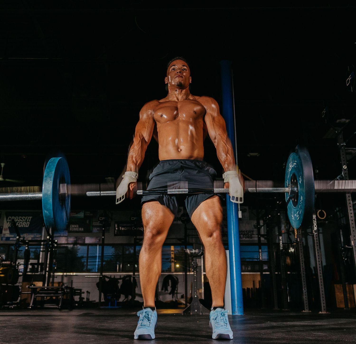Muscular shirtless man deadlifting heavy barbell in dark gym, showcasing strength and bodybuilding physique.