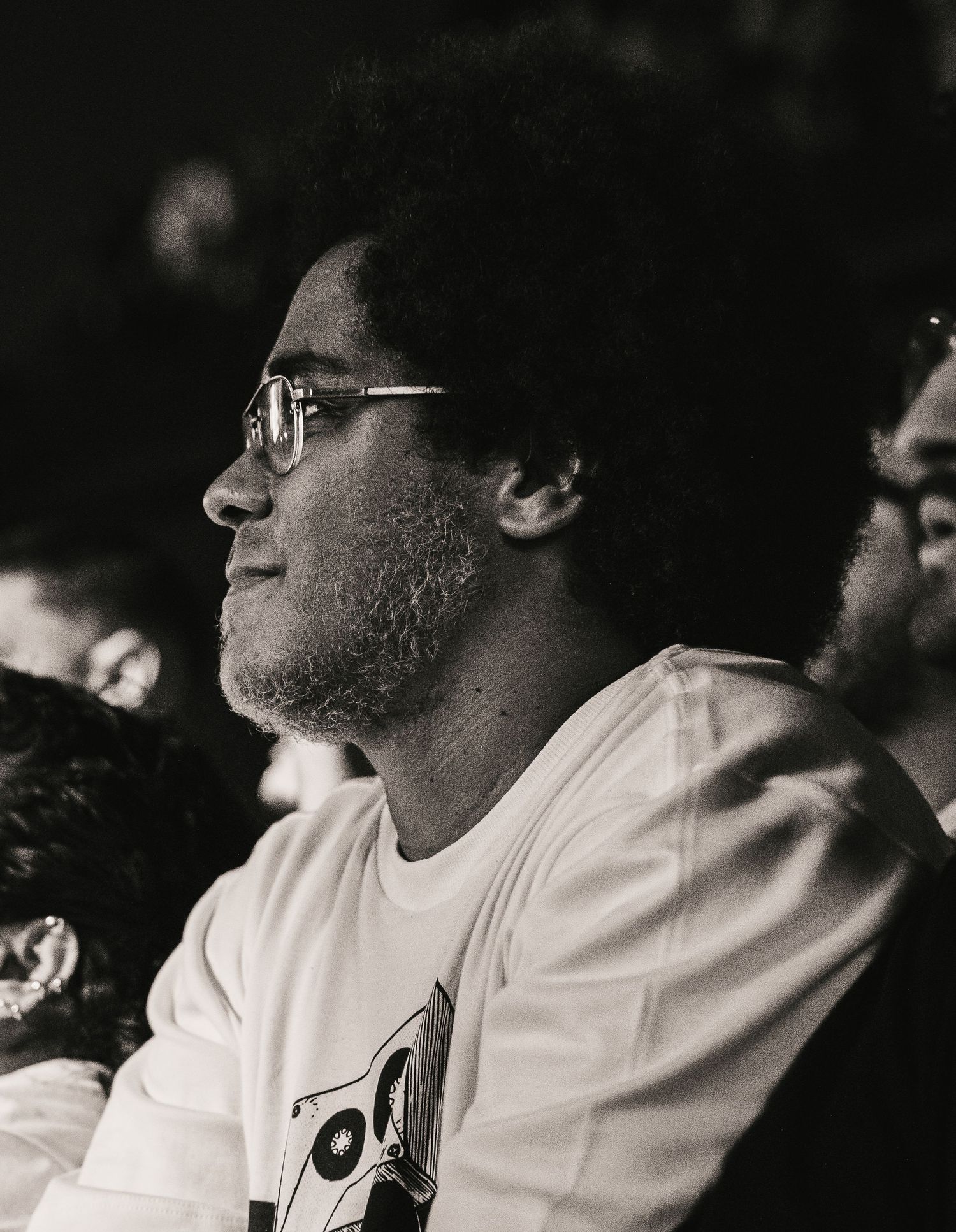 Black and white portrait of a young man with glasses and afro enjoying a live concert.