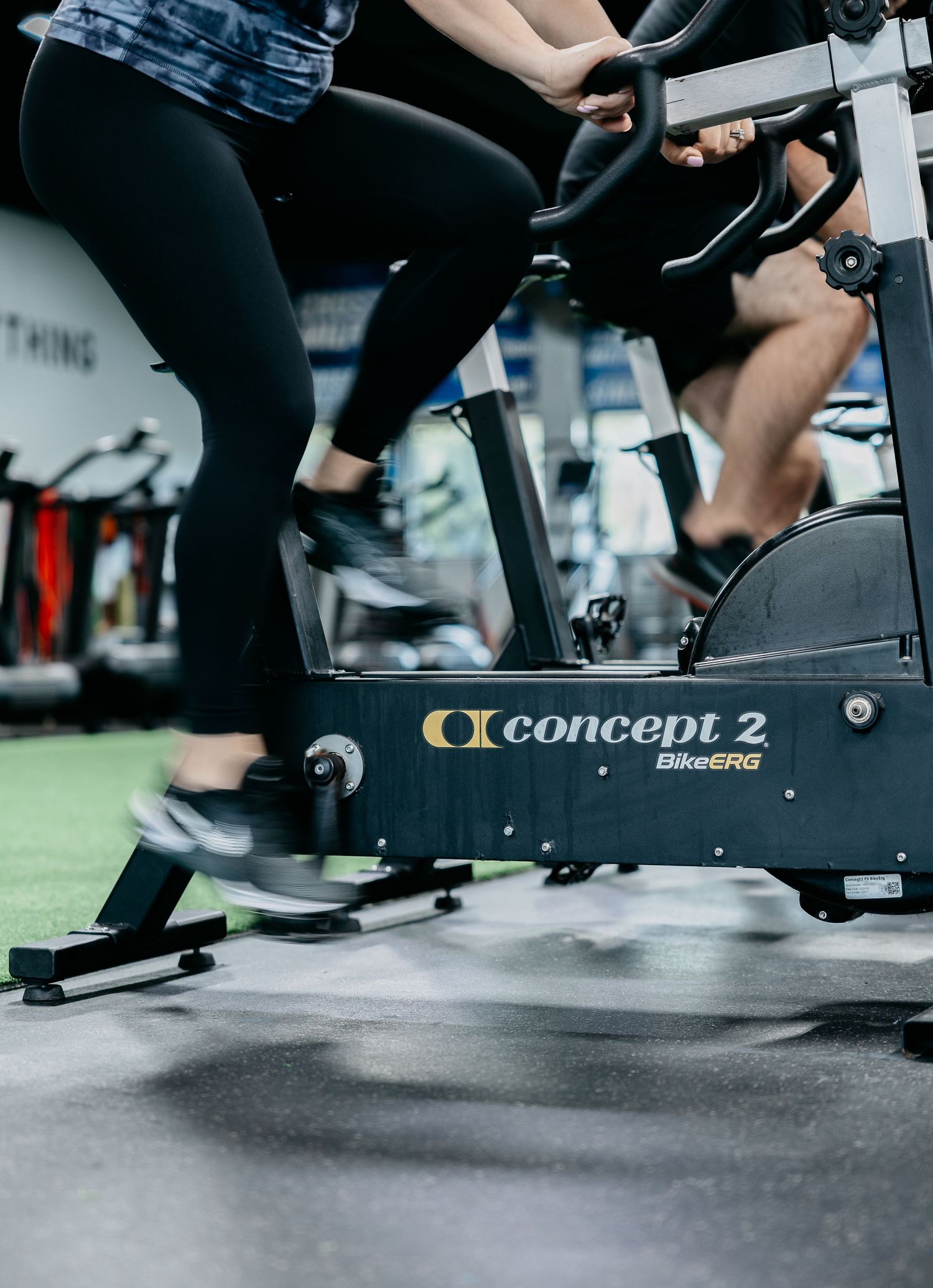 Two people exercising on Concept2 BikeERG stationary bikes in a modern gym setting.