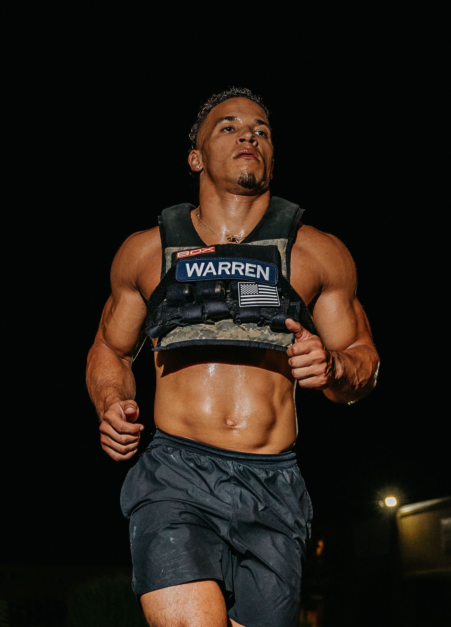 Muscular athlete named Warren runs outdoors at night wearing a weighted vest and gray shorts, showcasing a fit physique.