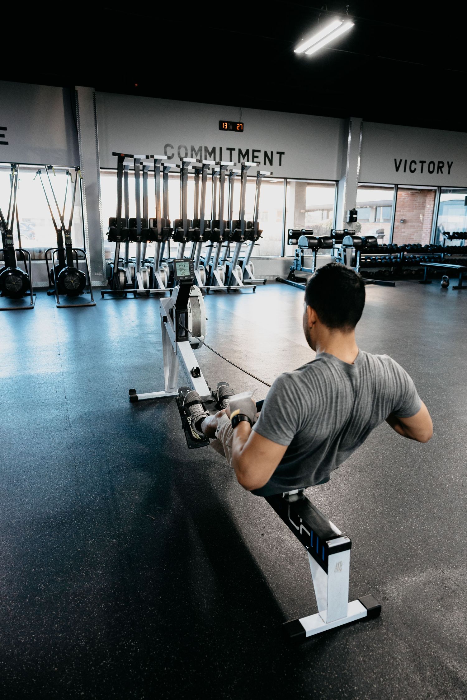 Man using a rowing machine in a modern gym with motivational words Commitment and Victory on the wall.