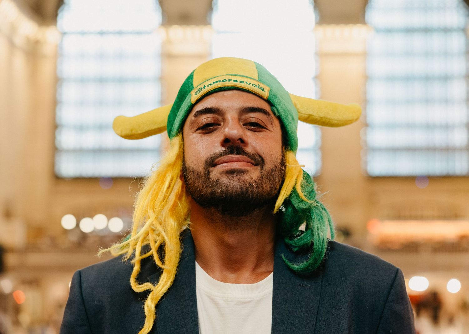 Bearded man wearing a festive green and yellow hat with braids at Grand Central.