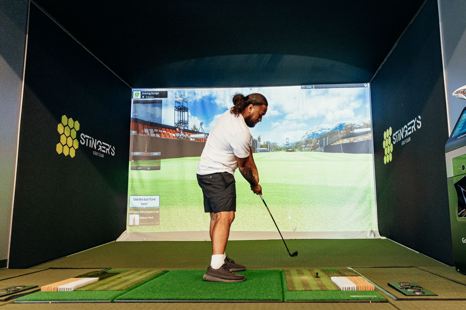 Man playing golf on an indoor simulator with a large screen displaying a virtual golf course.