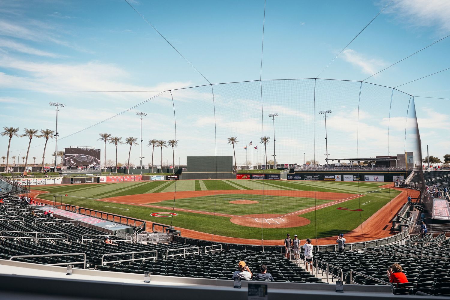 Wide-angle view of a baseball spring training stadium with palm trees under a blue sky.