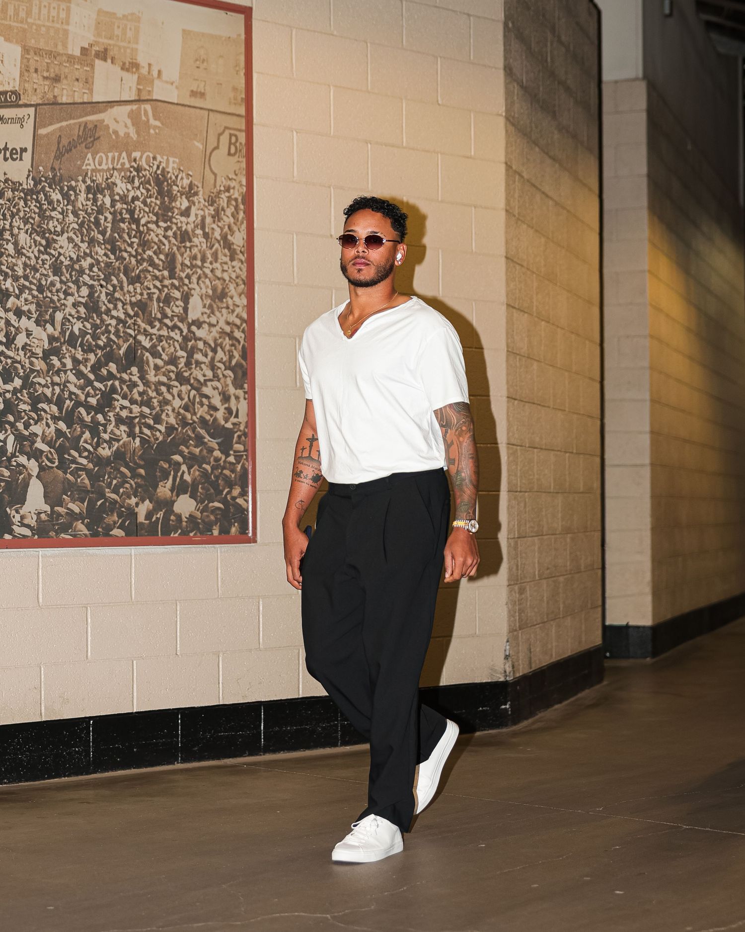 Tattooed male athlete in white t-shirt and black pants walks through arena corridor before a game.