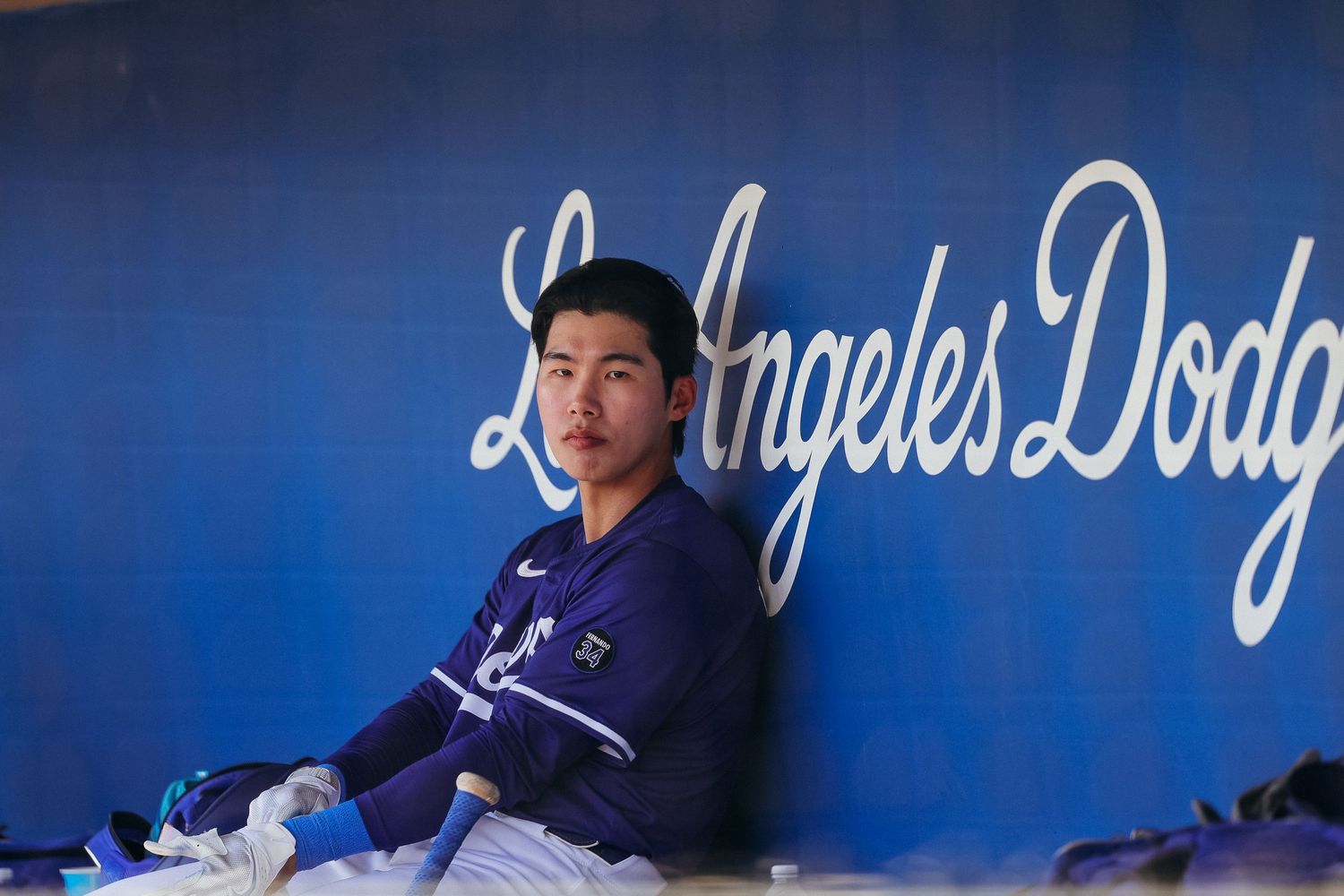 Los Angeles Dodgers player sitting pensively in the dugout in front of the team logo.