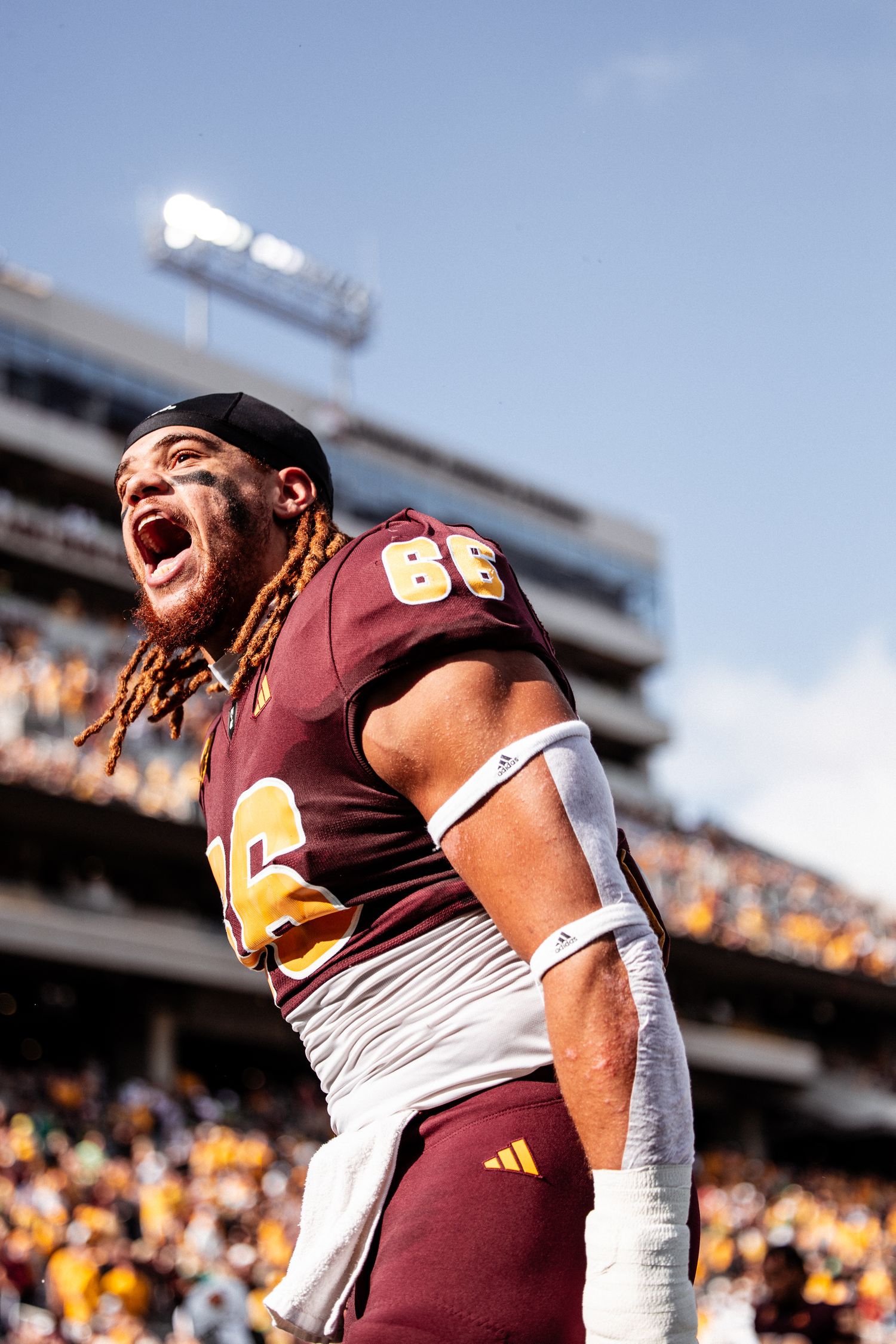 Arizona State Sun Devils football player number 66 with dreadlocks celebrates loudly on field in maroon uniform.