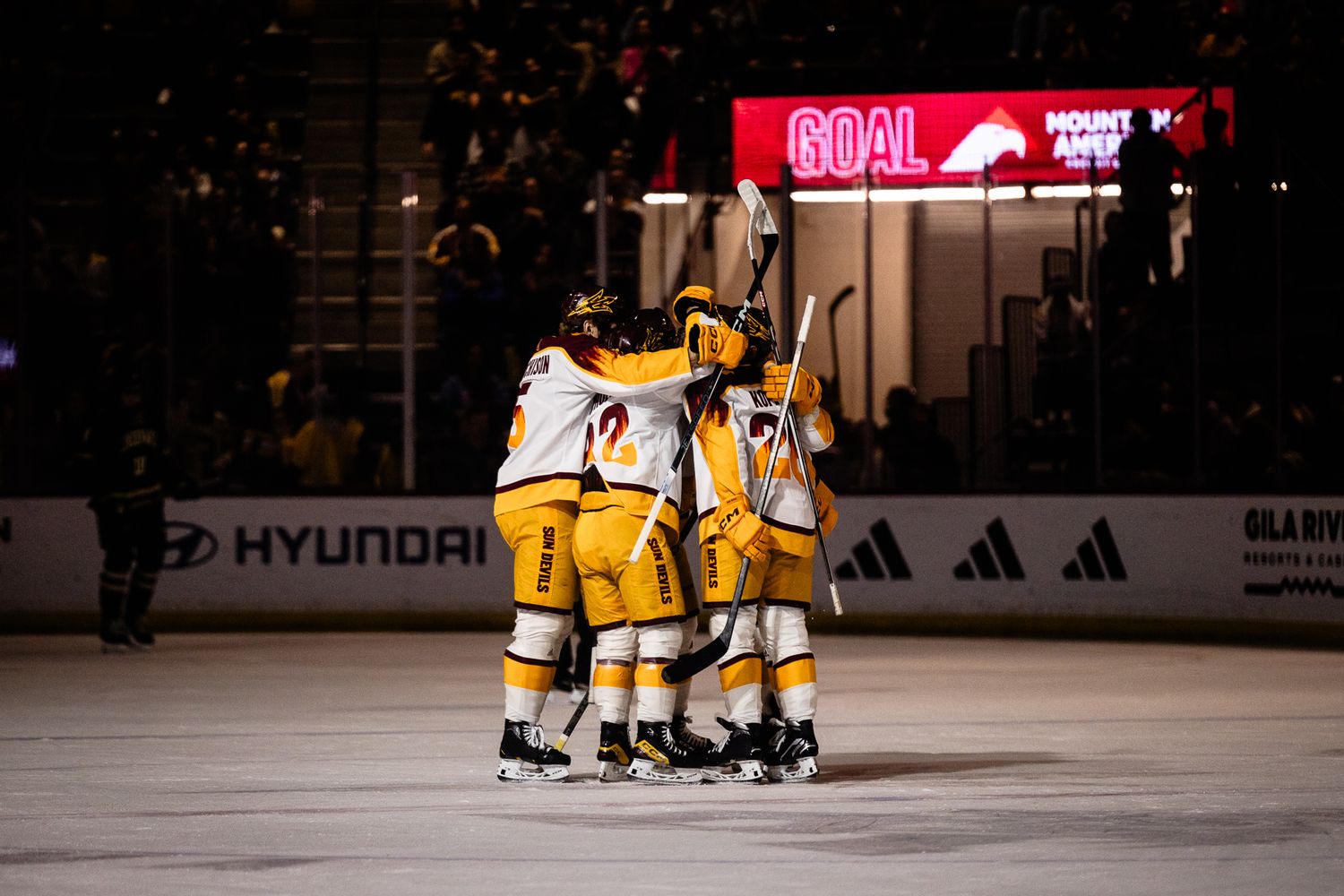 Arizona State Sun Devils hockey team celebrates a goal together on the ice under the scoreboard.