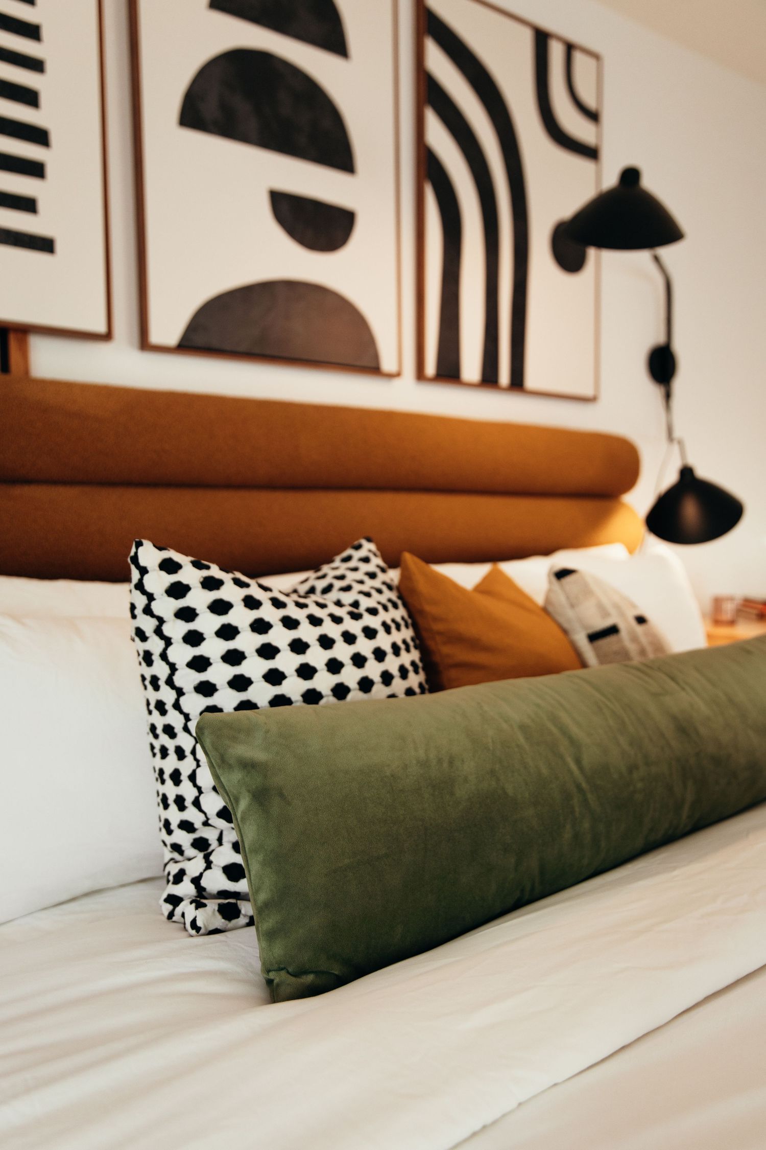 Stylish hotel bed with green velvet bolster, polka dot pillow, and abstract wall art above.