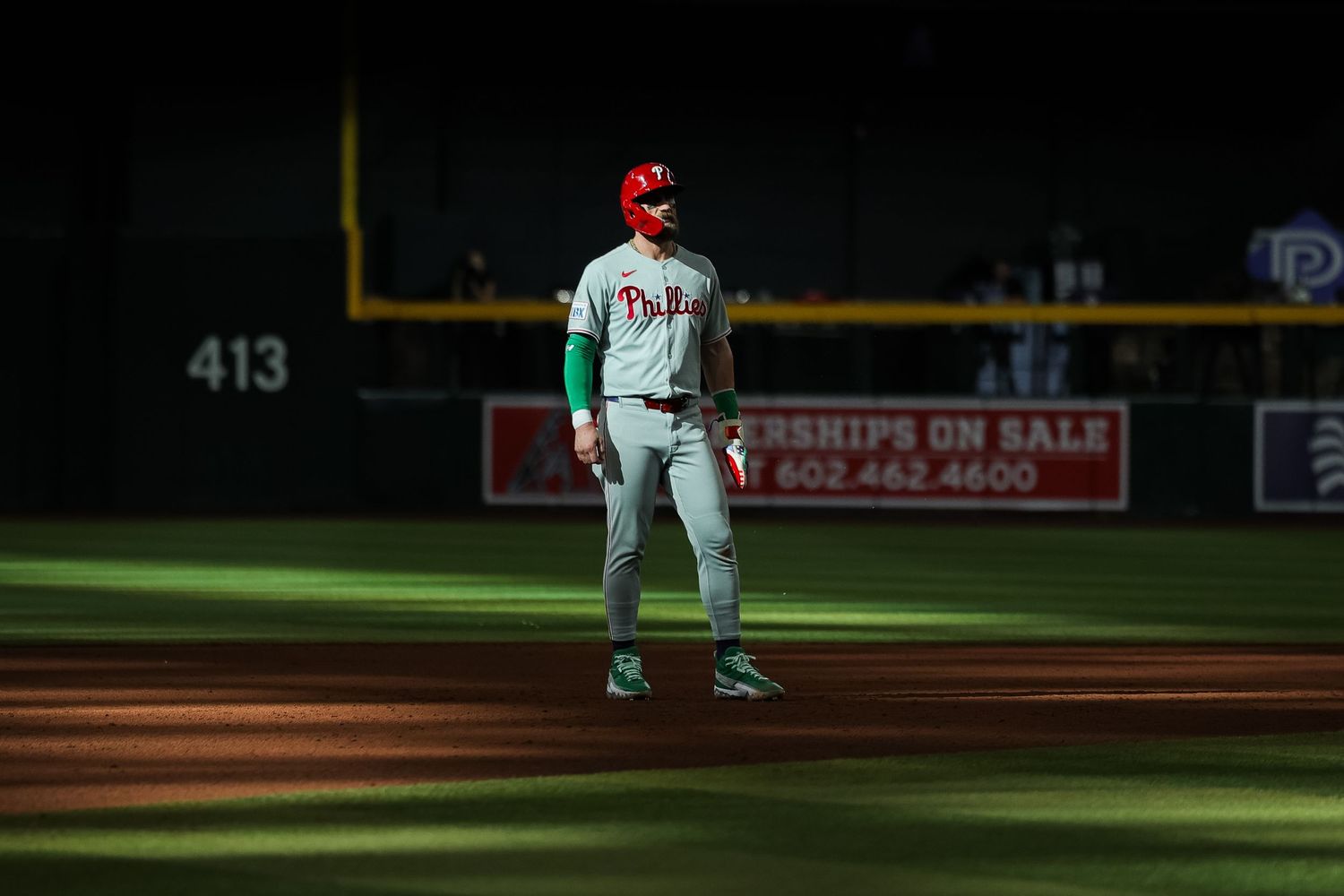 A Philadelphia Phillies player stands on the field at night during an away game.