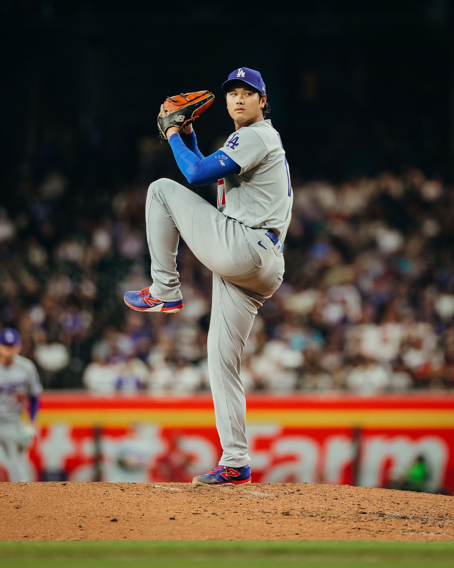 LA Dodgers pitcher in gray uniform delivering pitch with high leg kick on mound.