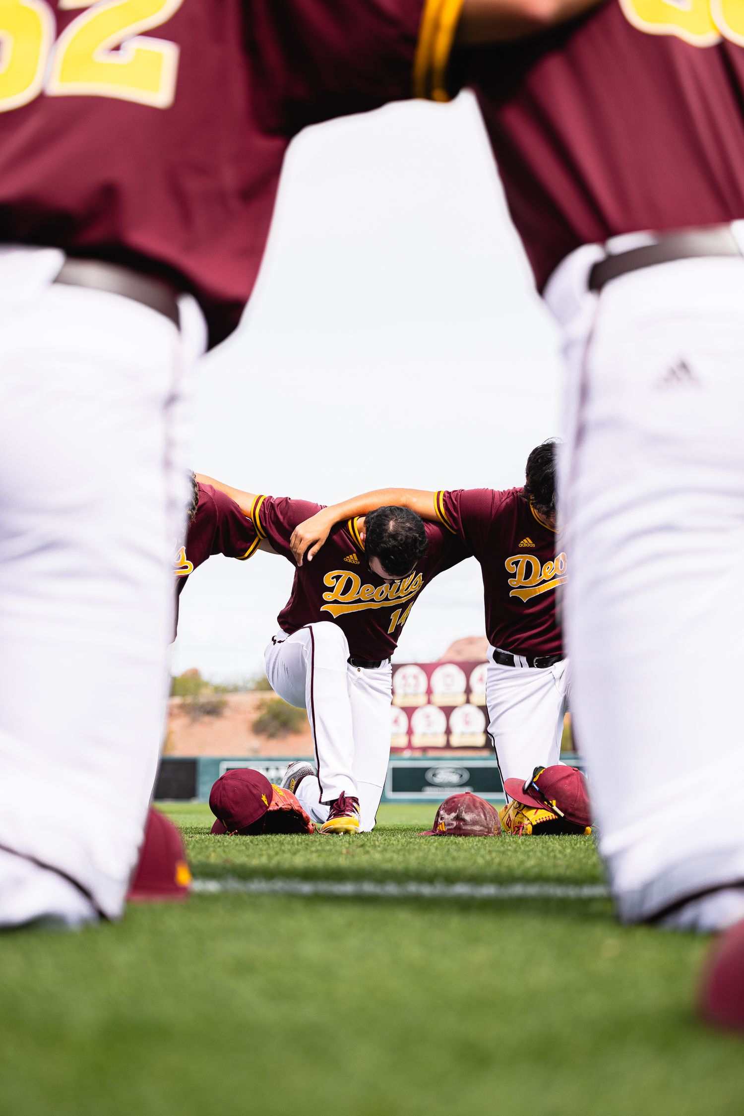 Arizona State Sun Devils baseball players huddle together in maroon Devils uniforms on the field before a game.