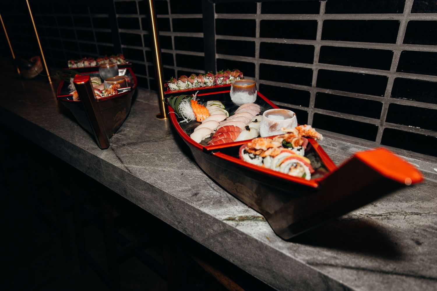 Assorted sushi rolls elegantly displayed in a red wooden boat on a dark surface.
