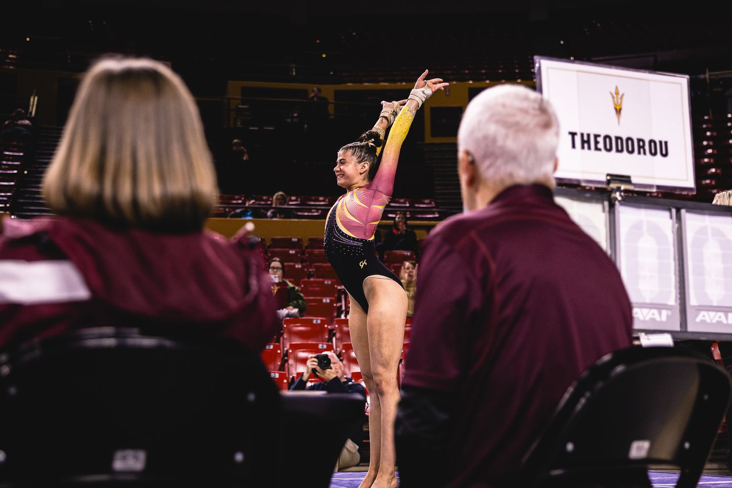 ASU gymnast performs floor exercise as judges observe with a Theodorou scoreboard visible.