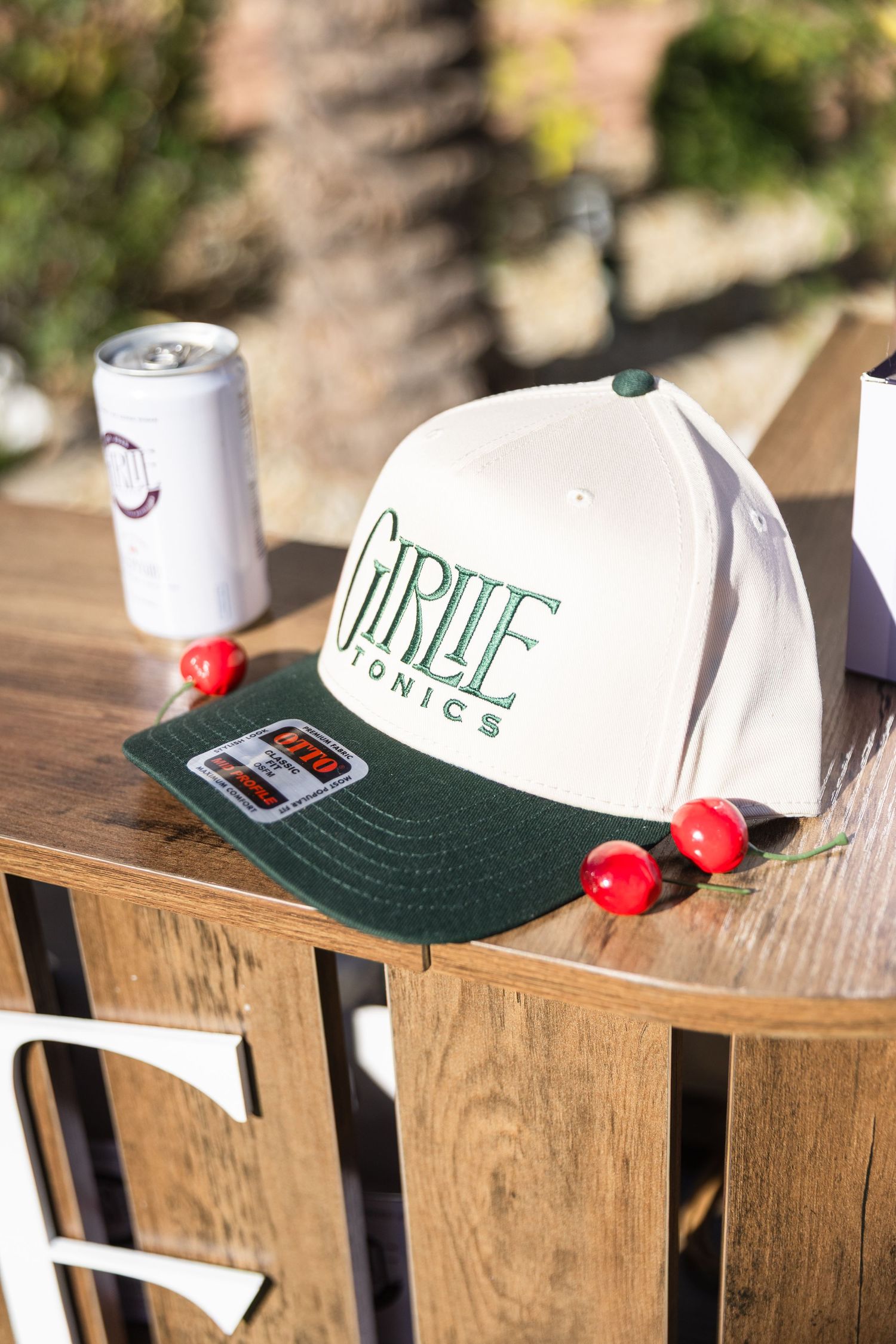 White and green Girlie Tonics snapback hat displayed on a wooden surface outdoors.