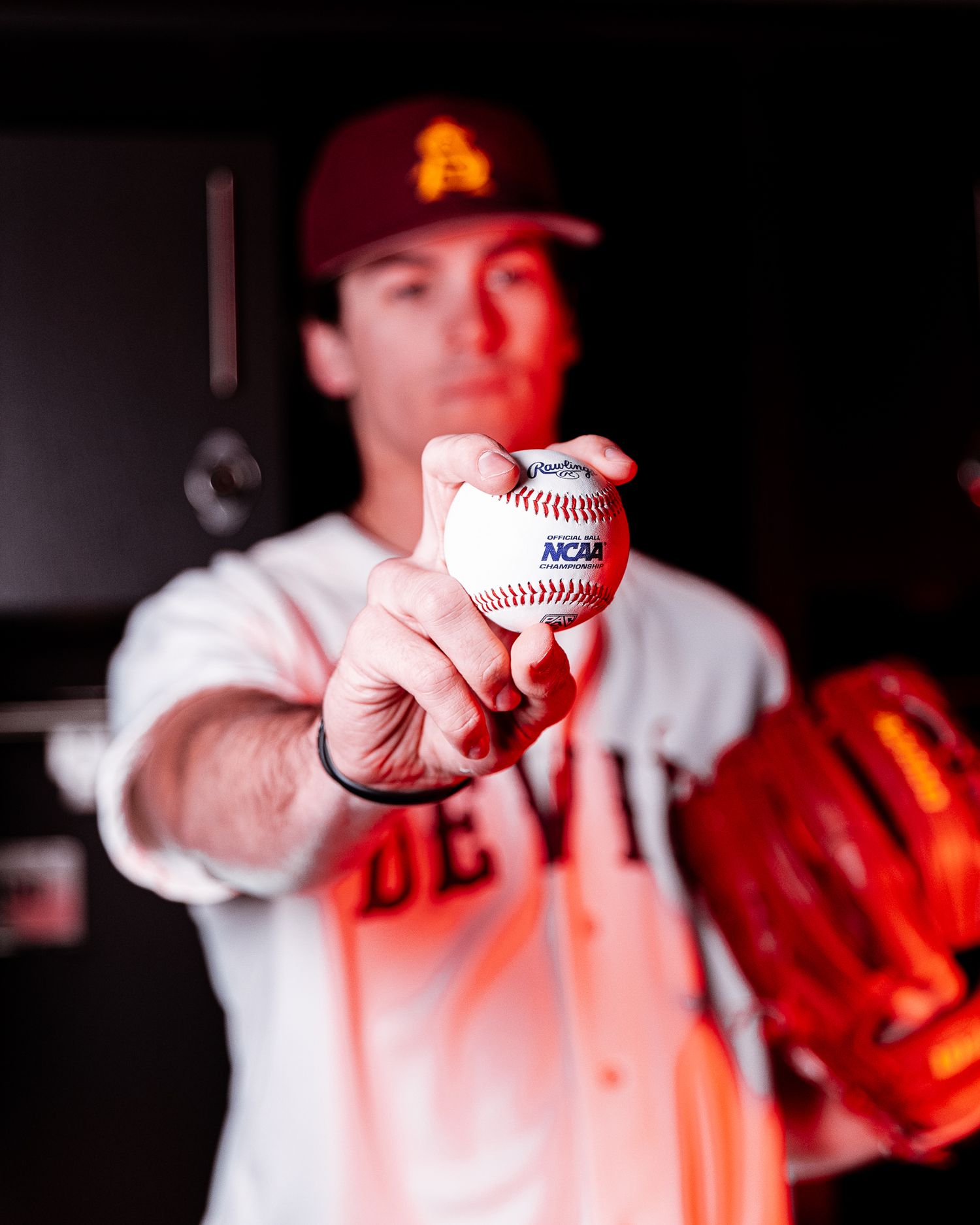 Arizona State Devils baseball player holds an NCAA baseball toward the camera in the dugout.