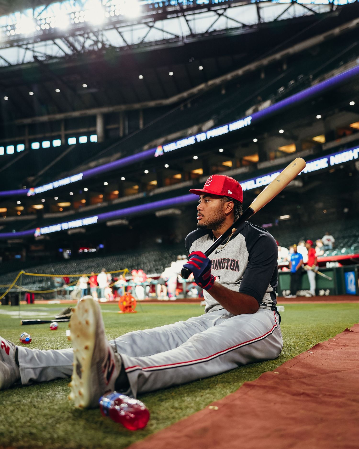 Washington Nationals player sits on field holding a bat during pre-game warmups inside a stadium.
