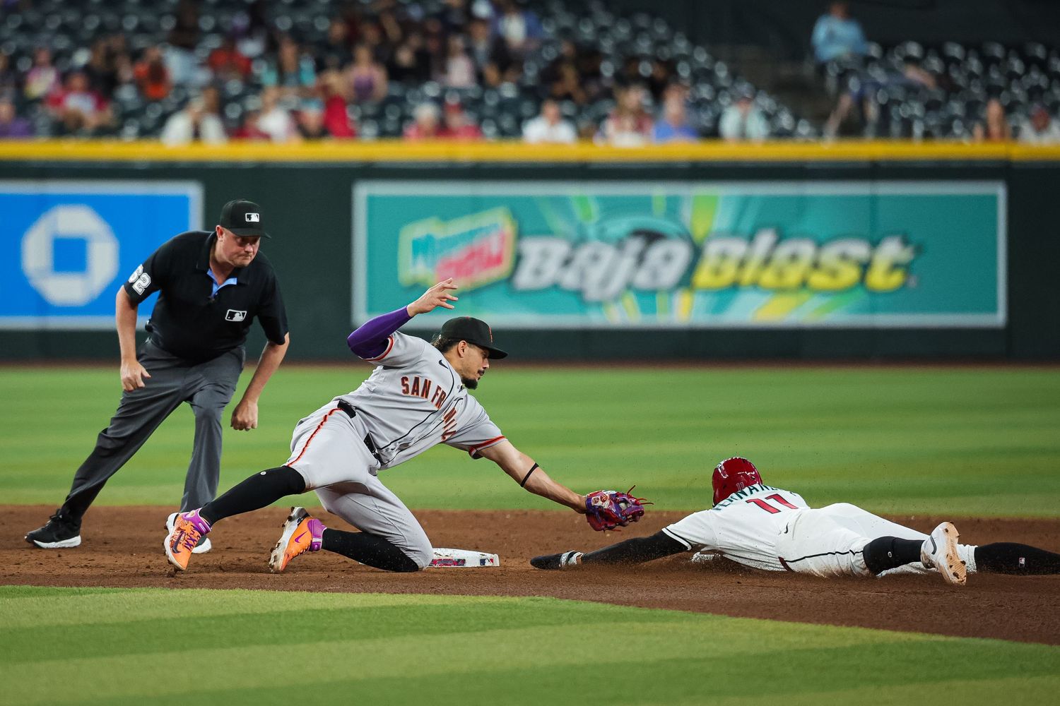 Baseball player tags out a sliding runner at second base as an umpire watches closely during an MLB game.
