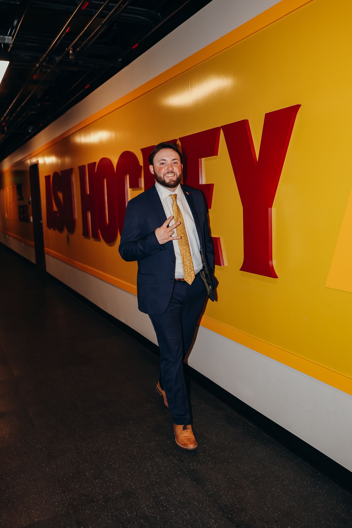 Man in navy suit with gold tie posing in front of ASU Hockey wall mural.