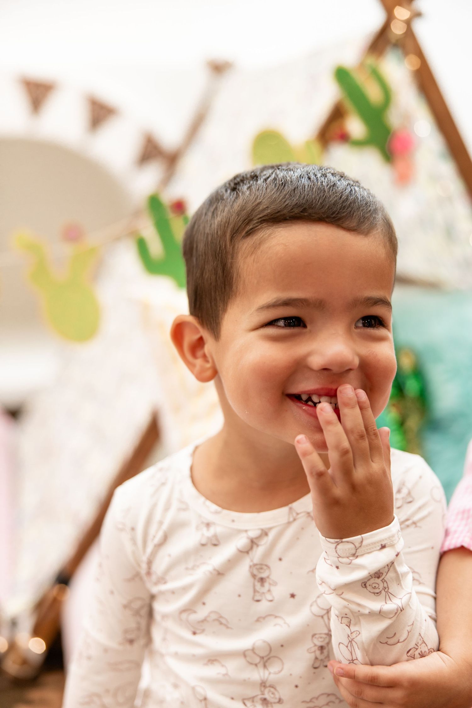 Cute smiling toddler boy in white pajamas at a boho-themed birthday party.