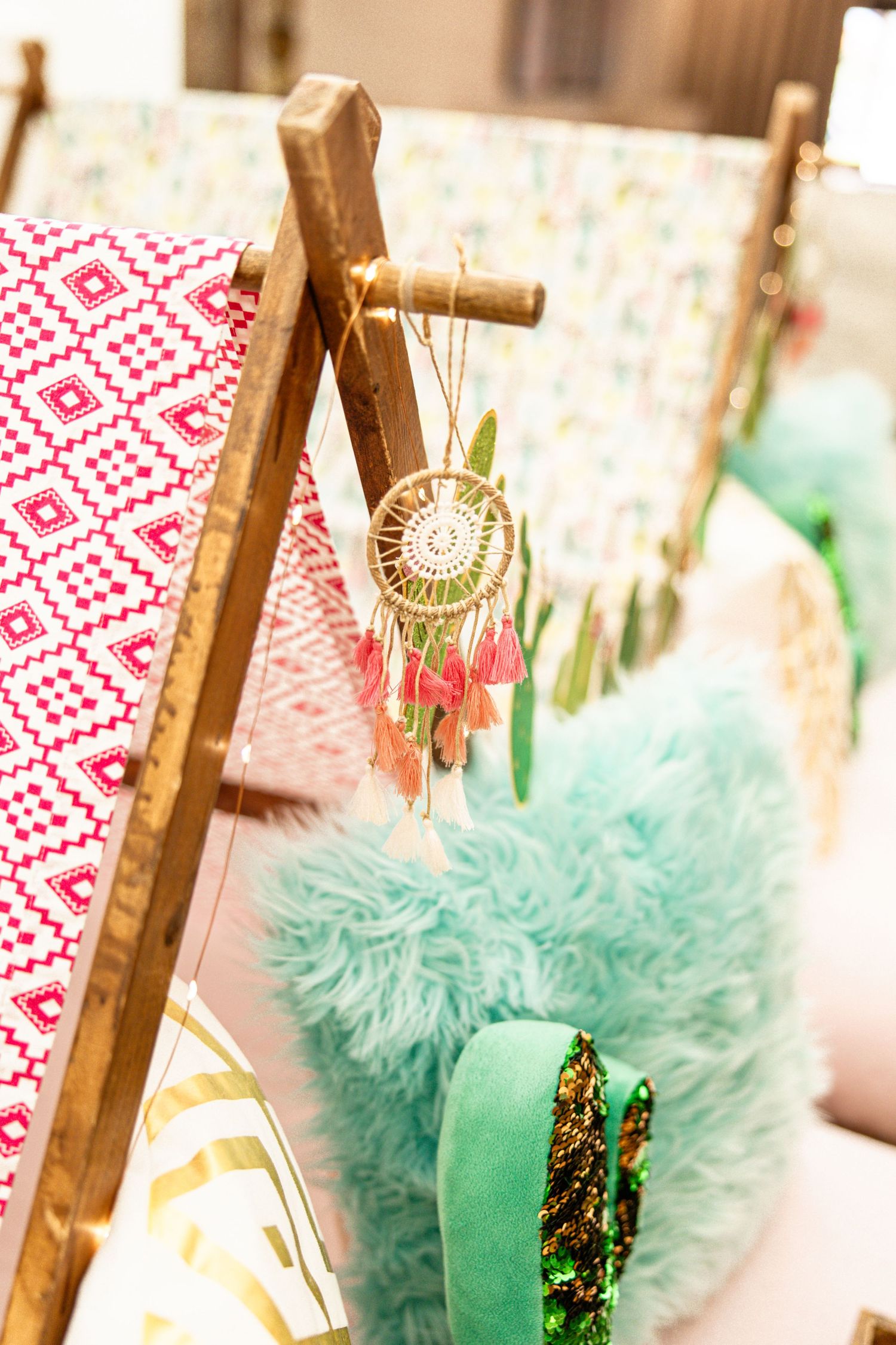 Boho dreamcatcher with pink tassels hanging on wooden teepee frame with colorful pillows.
