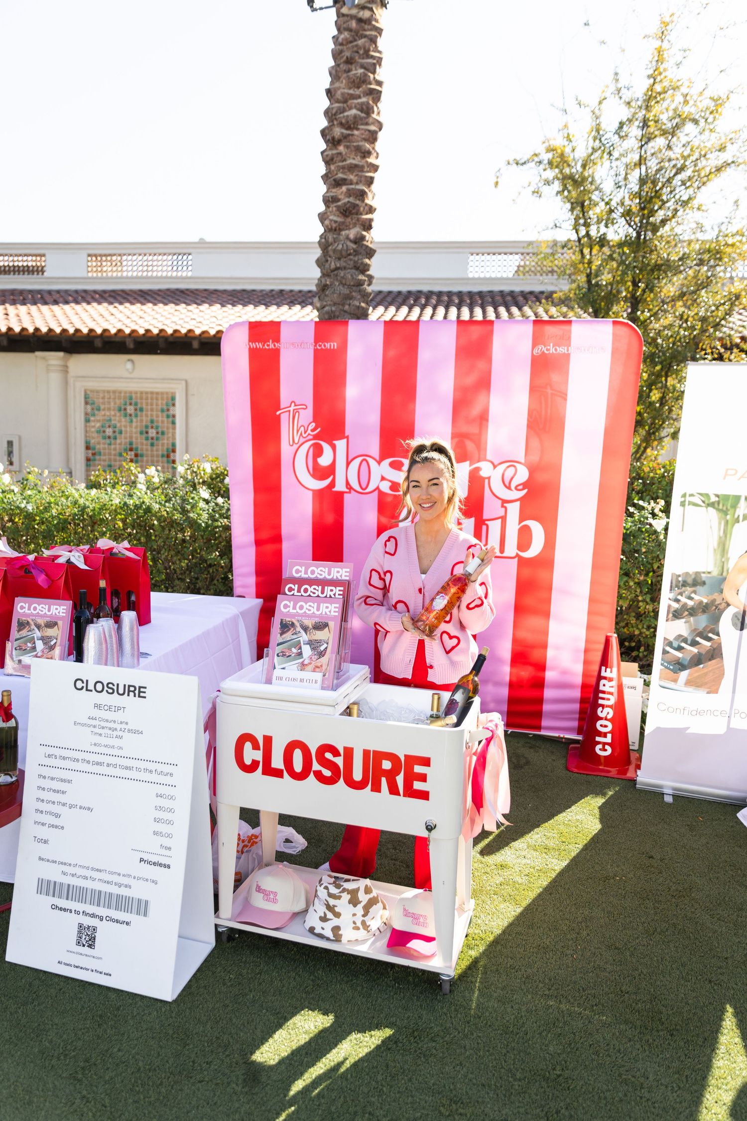 Woman stands at a vibrant red and white striped Closure Club pop-up booth with branded merchandise display.