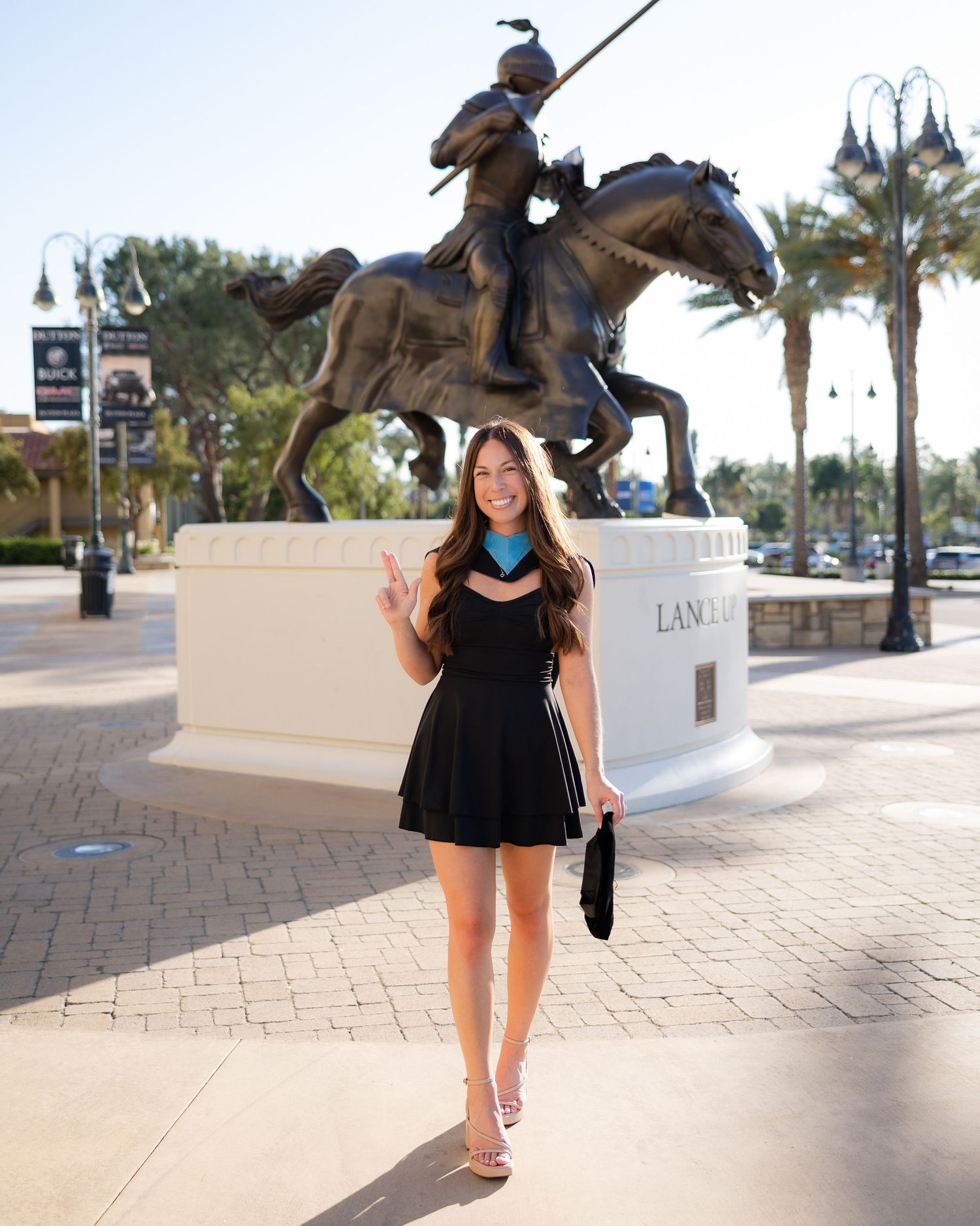 Woman in black mini dress posing in front of a bronze equestrian statue at a Lancaster shopping plaza.