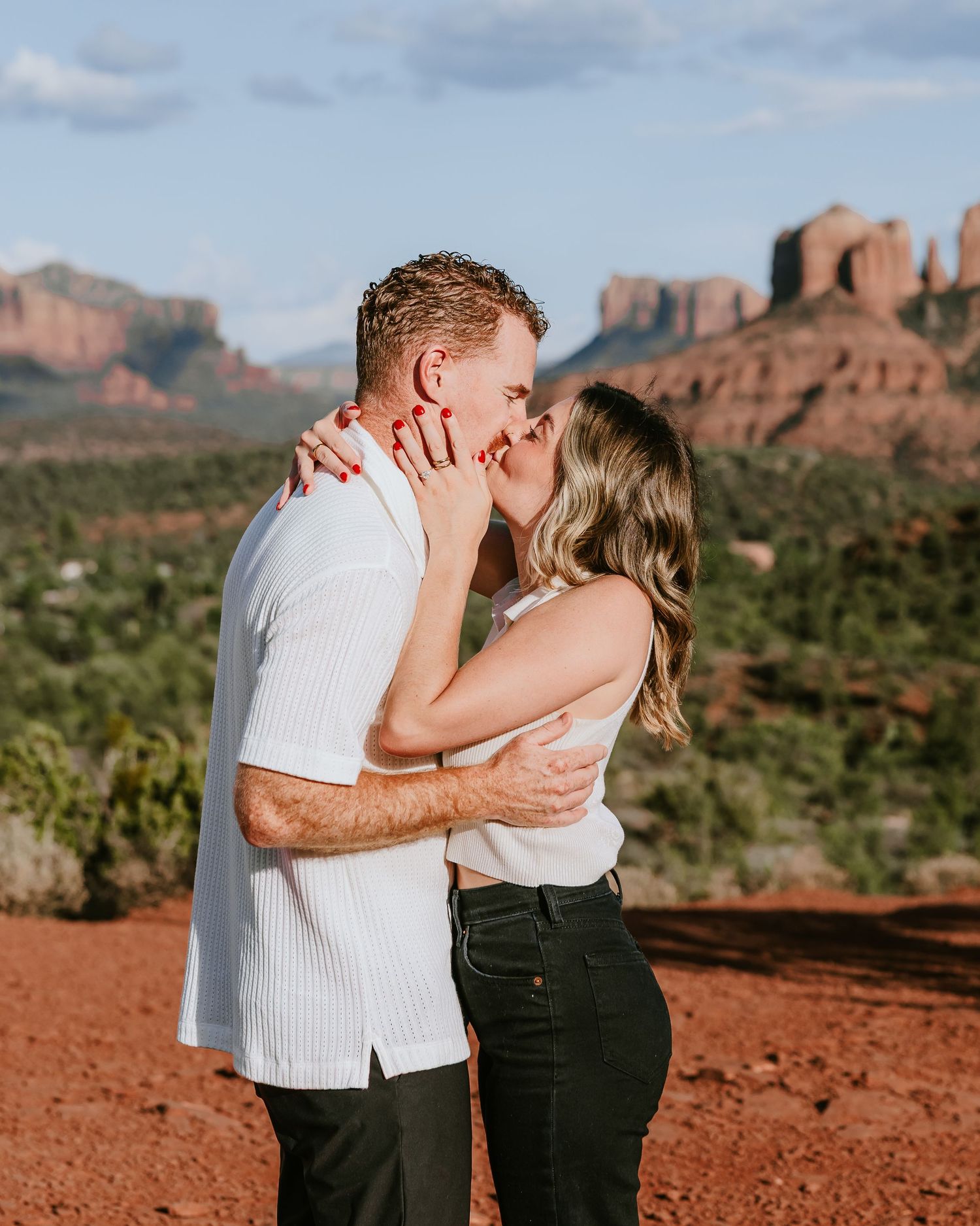 Couple kissing at sunset in Sedona, Arizona, with red rock formations and desert landscape in the background.